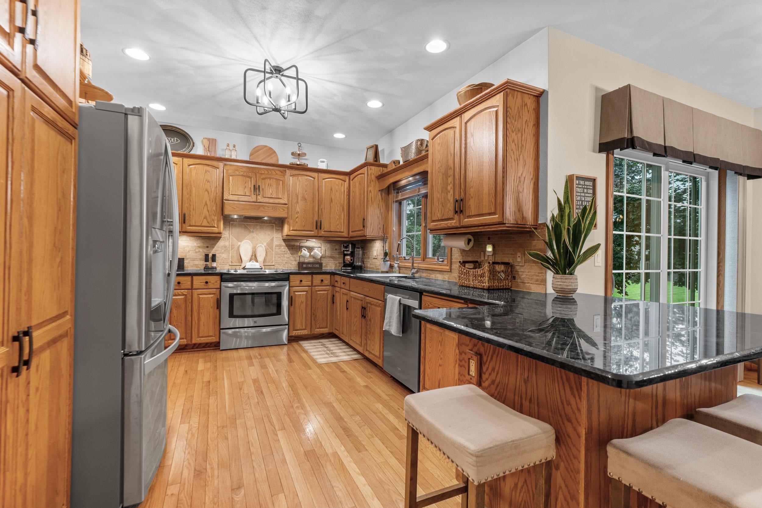Kitchen with oak cabinets, black granite counters, stainless steel appliances, and a hardwood floor.