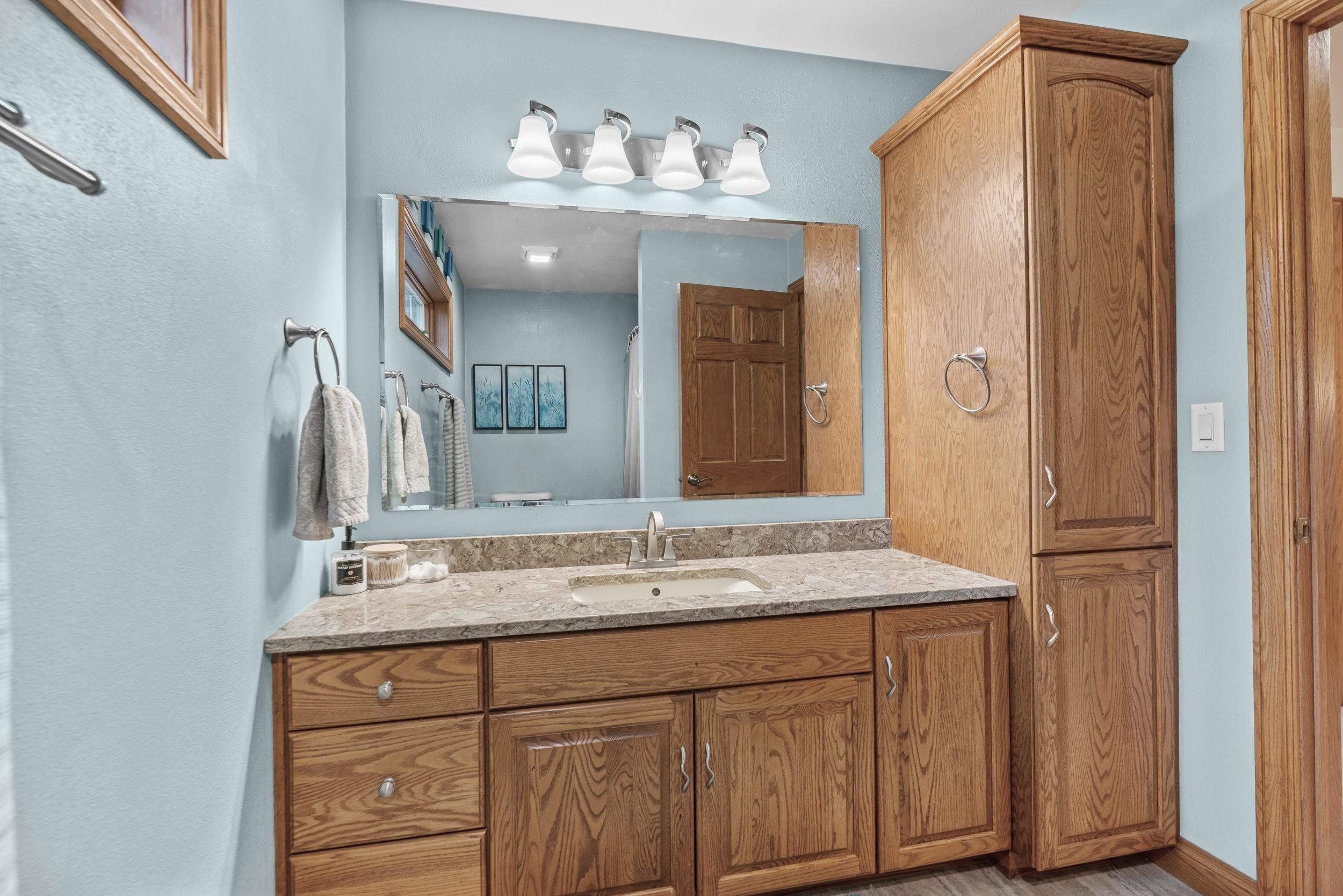 Bathroom with an oak vanity, stone countertop, large mirror, and matching tall storage cabinet.