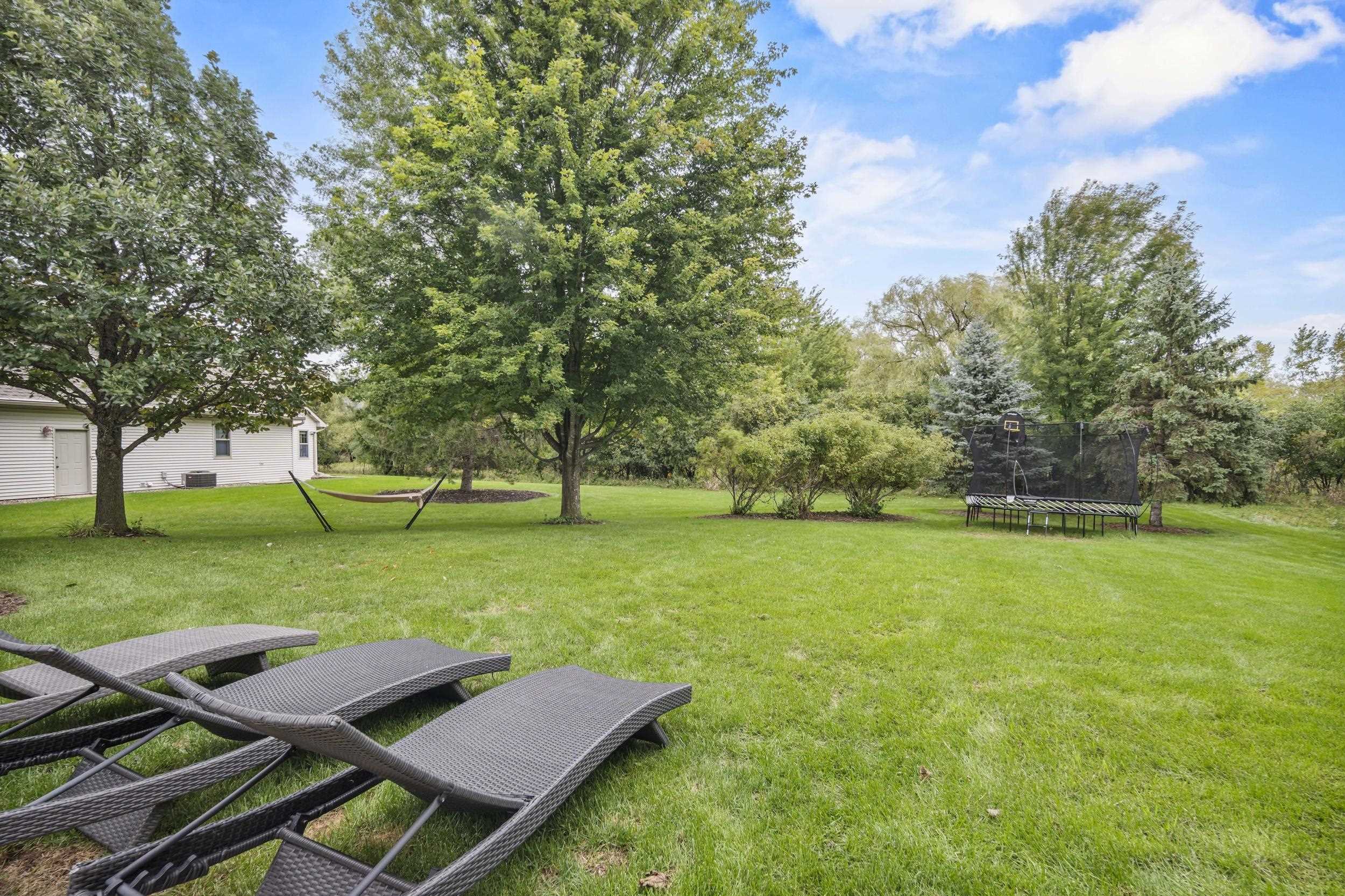 Spacious backyard with mature trees, a hammock, trampoline, and woven chaise lounges.