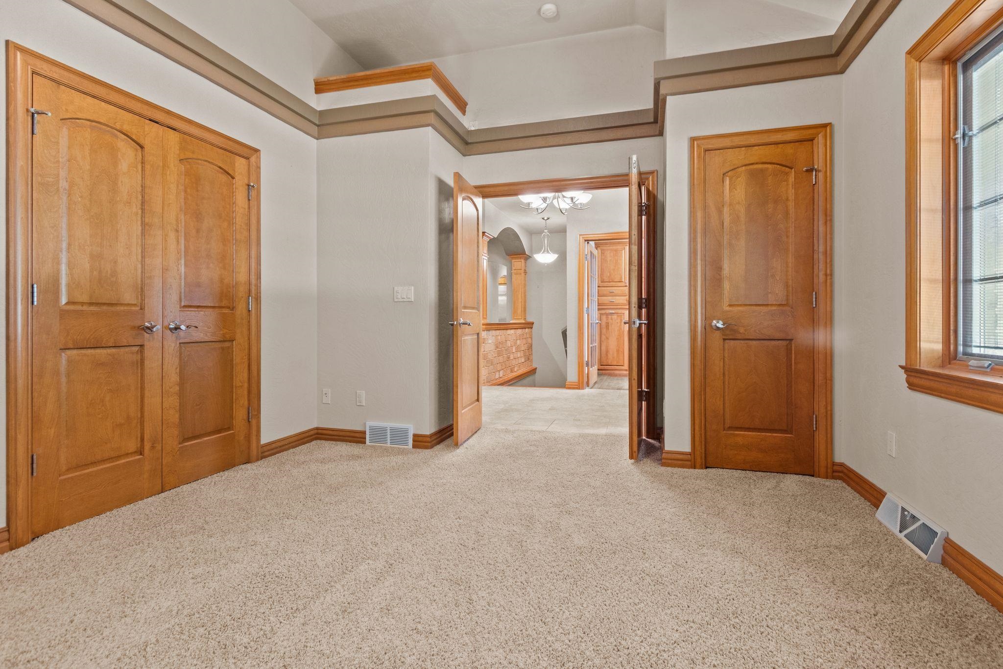 Empty carpeted bedroom with a wooden double-door closet and warm wood trim.