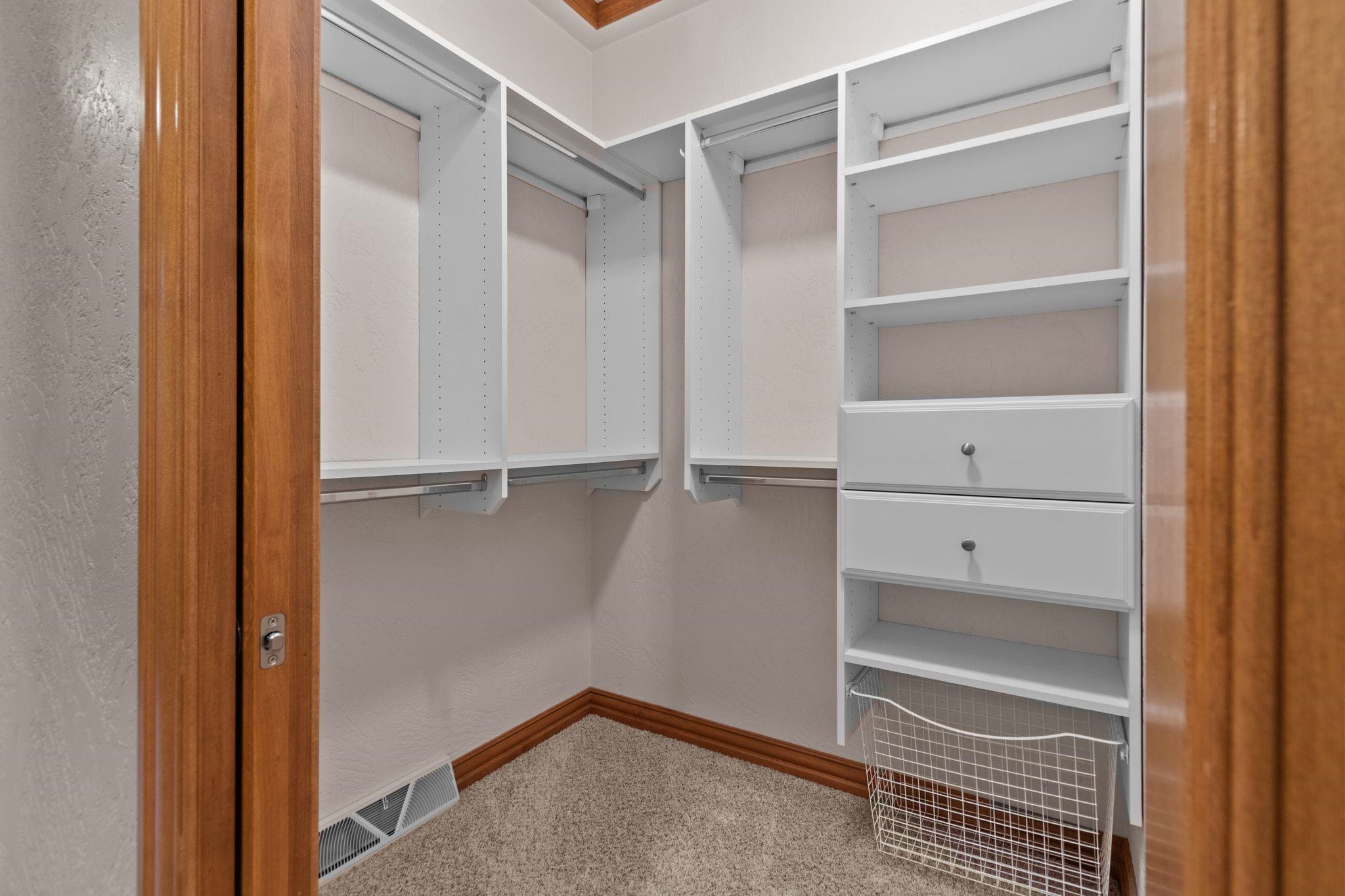 Walk-in closet with white built-in shelves, hanging rods, drawers, and a wire basket.