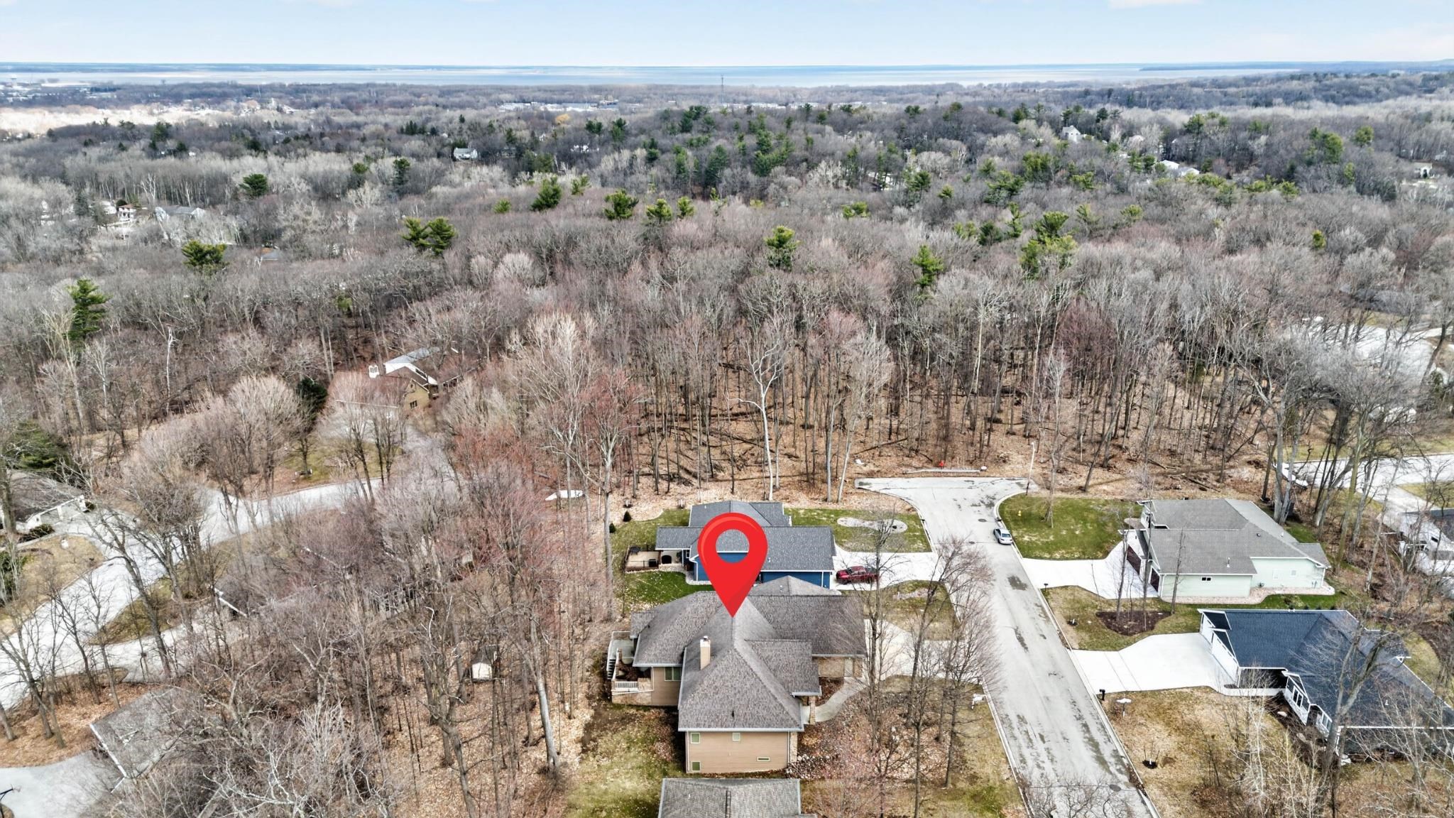 Aerial view of a wooded home marked by a red pin, with water visible in the distance.