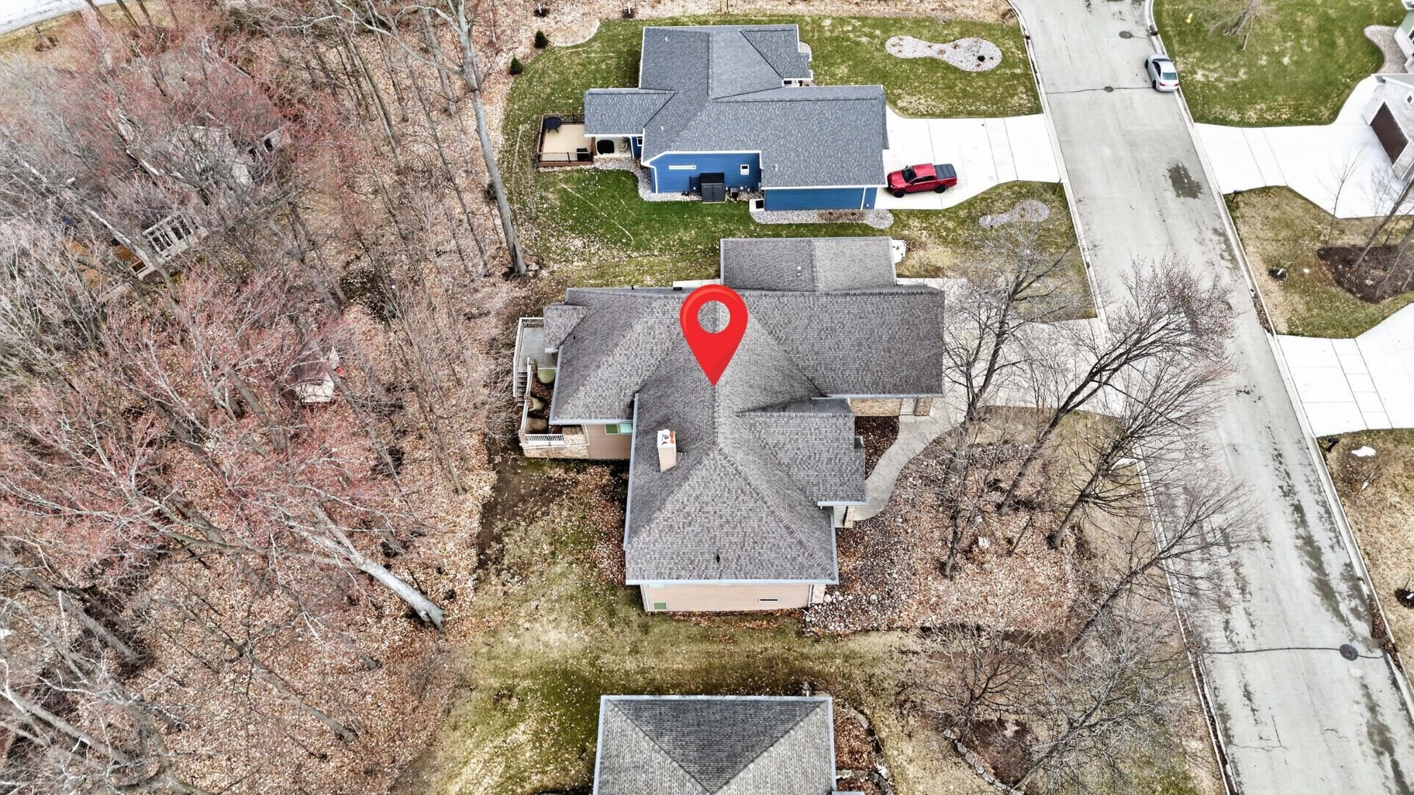 Aerial view of a gray-roofed house marked with a red location pin, beside a residential street.
