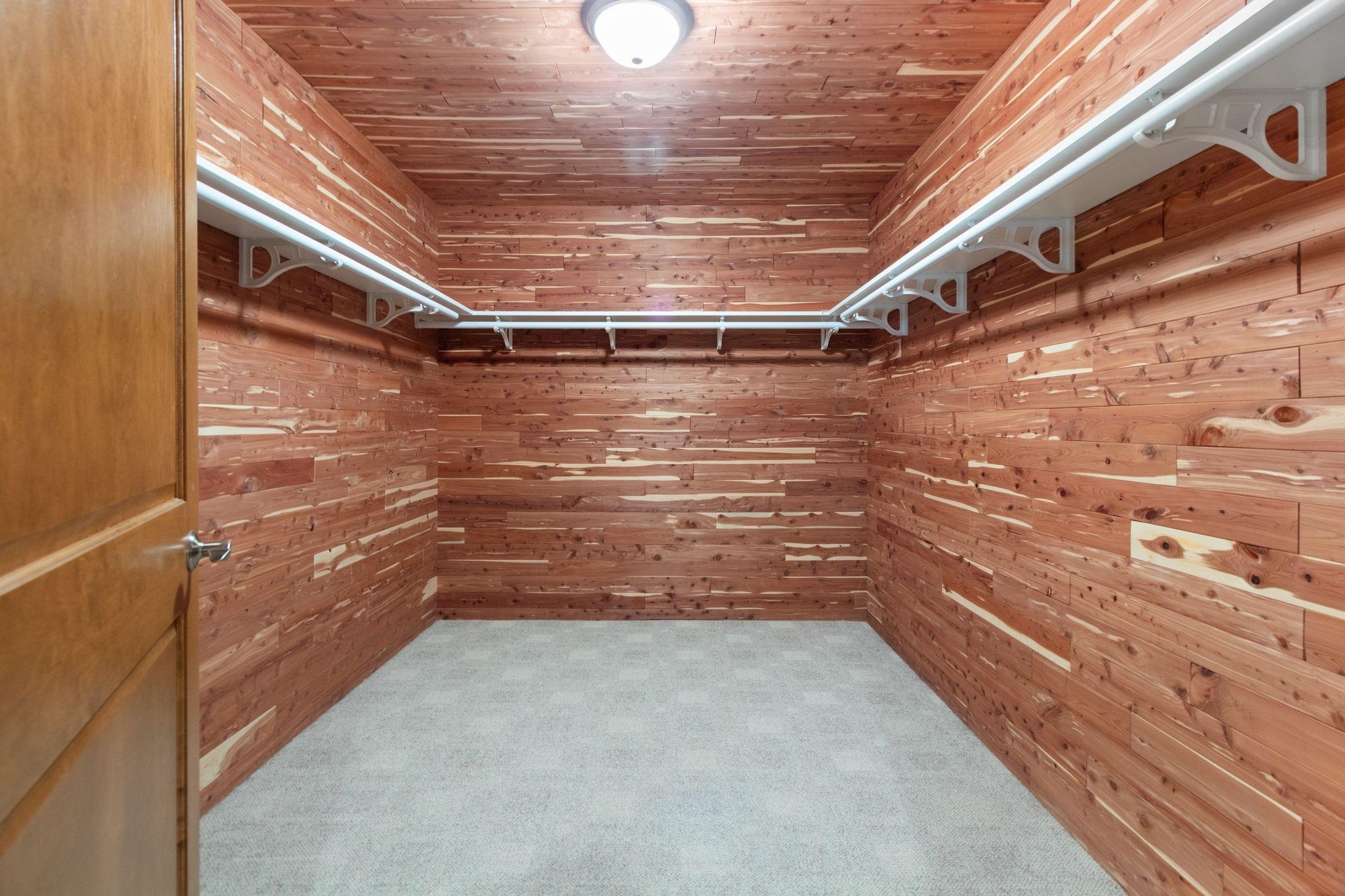 Empty walk-in closet with cedar walls and ceiling, white hanging rods, and light gray carpet.
