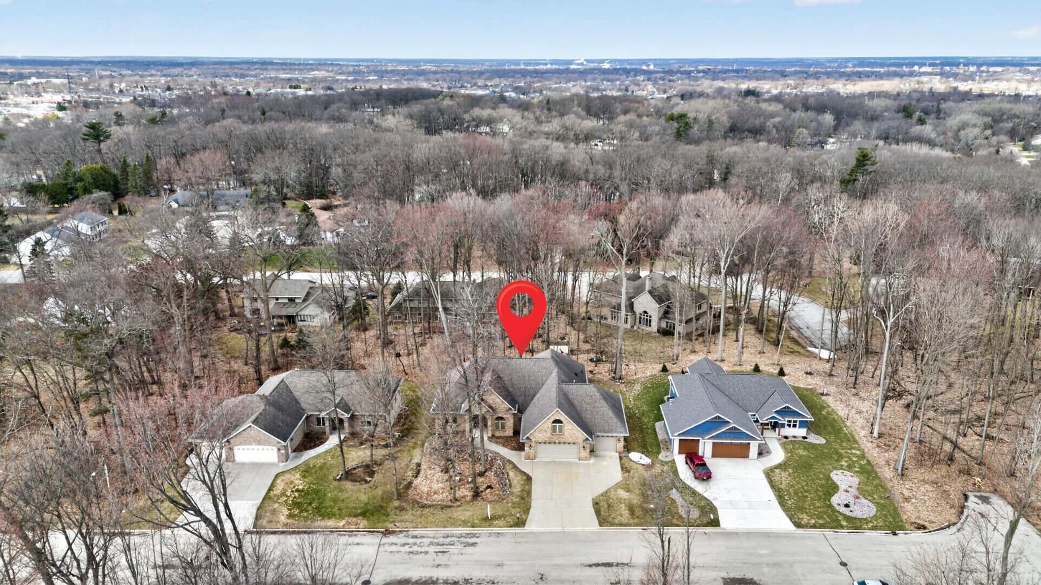 Aerial neighborhood view with a red pin marking a home among leafless trees.