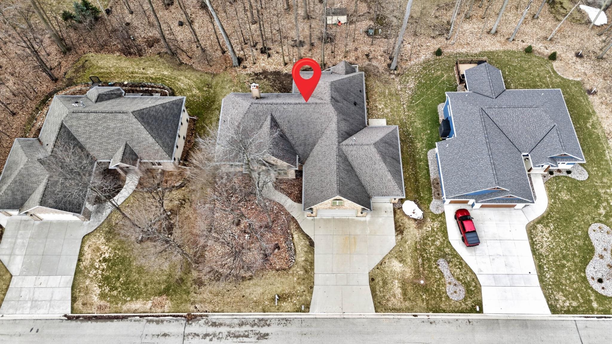 Aerial view of a home marked by a red pin, with neighboring houses and a wooded backyard.