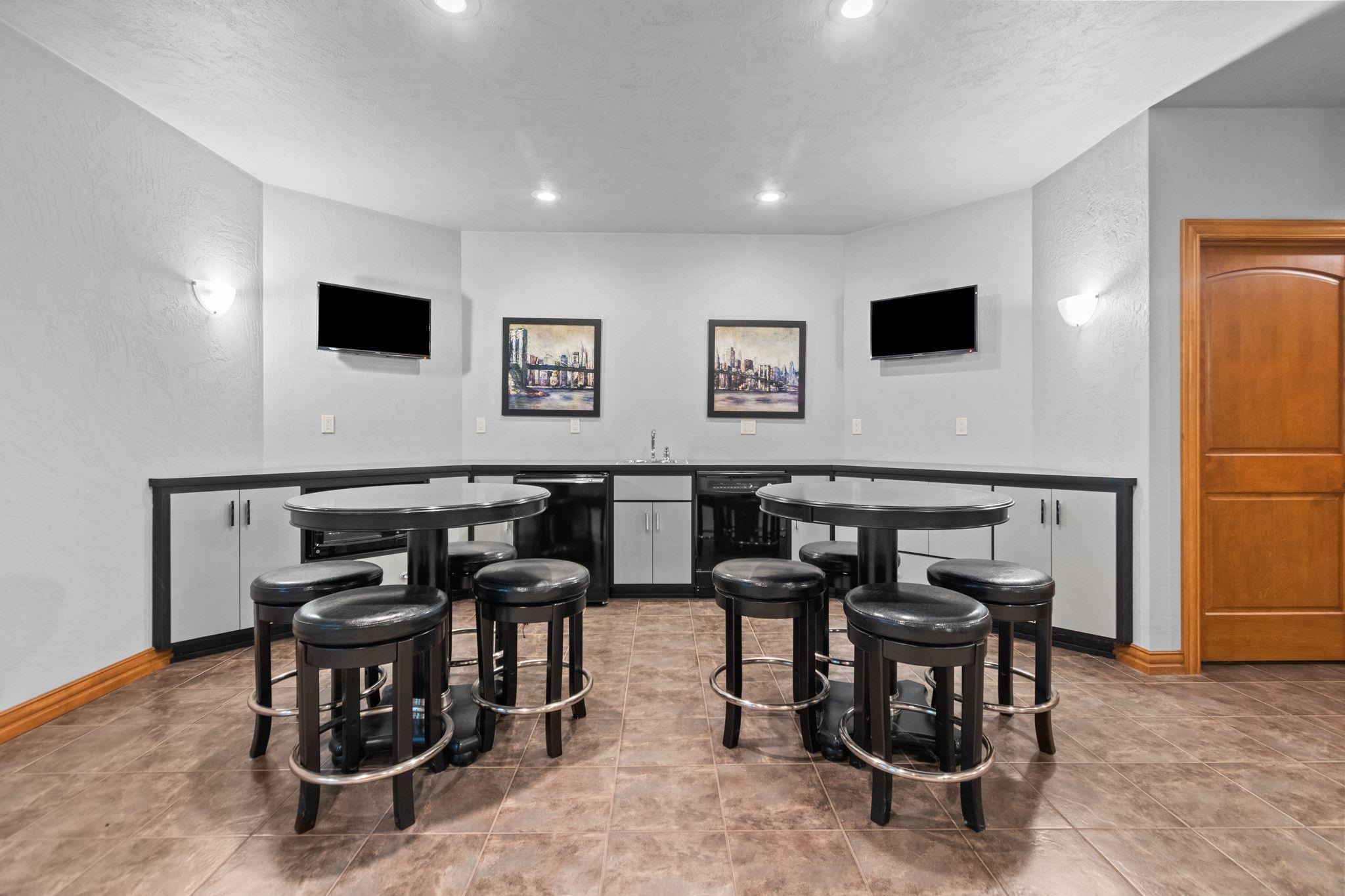 Recreation room with pub tables and stools, built-in cabinets, and two wall-mounted televisions.