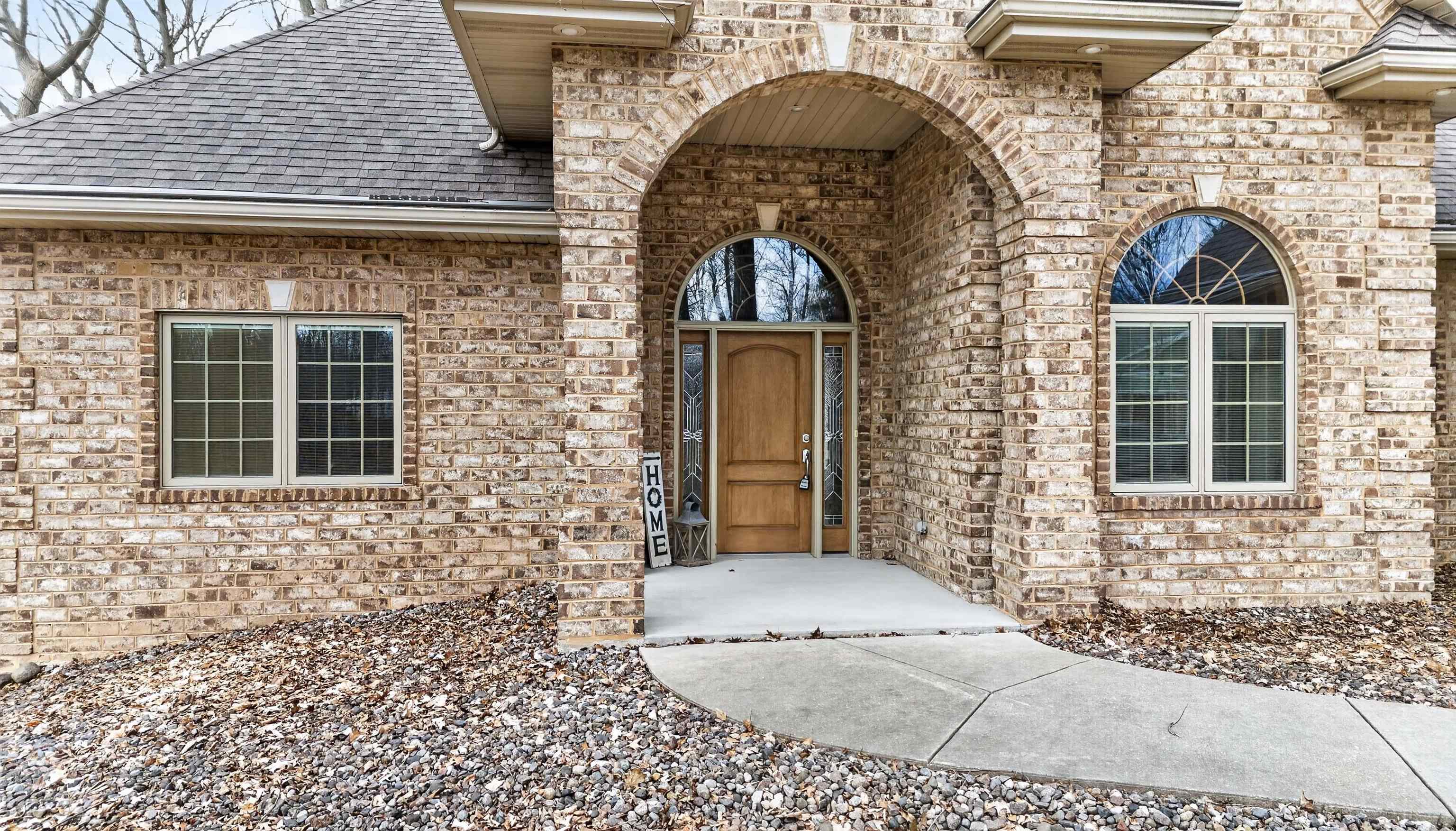 Brick home entrance with an arched porch, wooden door, arched windows, and curved walkway.