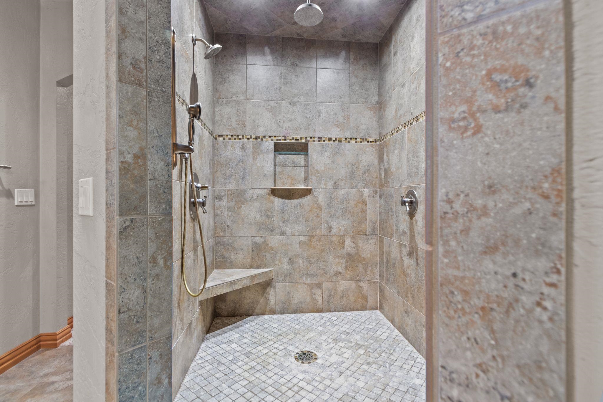 Walk-in shower with stone-look tile, multiple shower fixtures, a built-in bench, and mosaic floor.