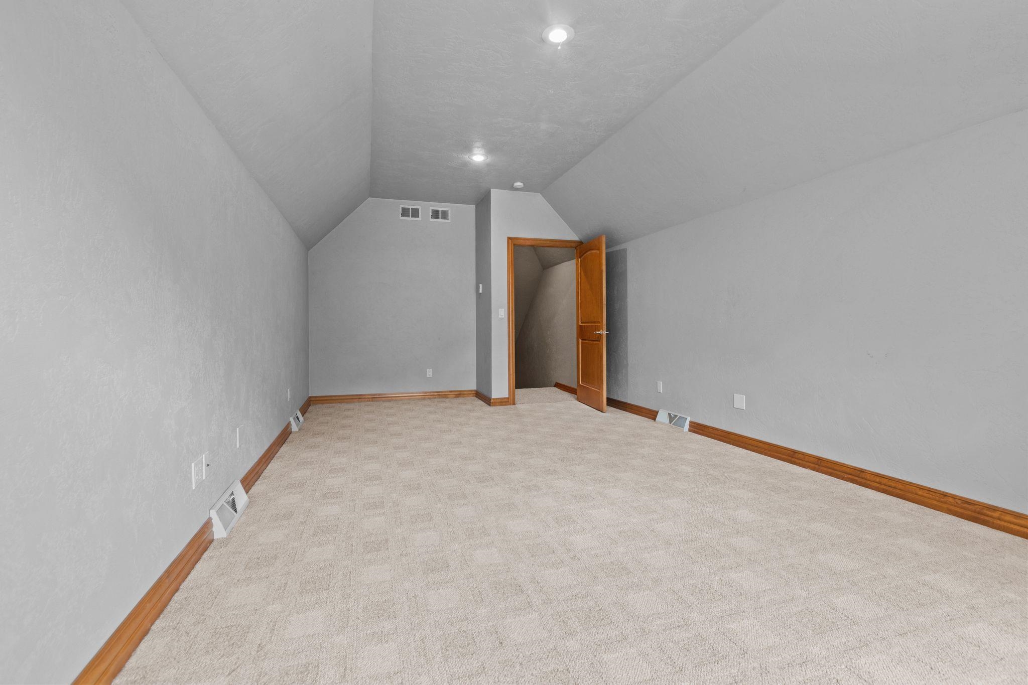 Empty carpeted room with a high sloped ceiling and an open wooden door.