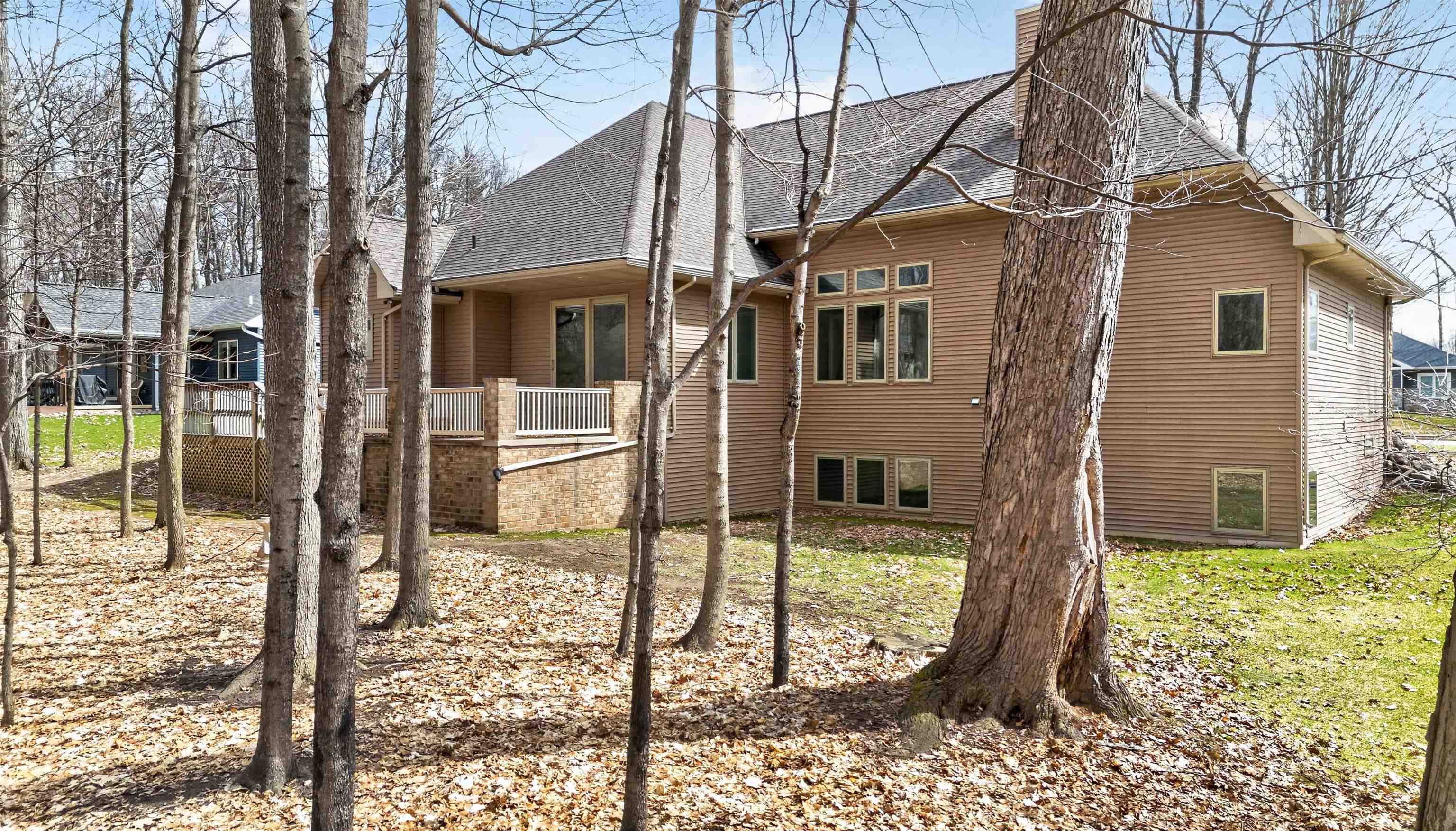 Rear of a brown-sided house with a raised deck among mature leafless trees.