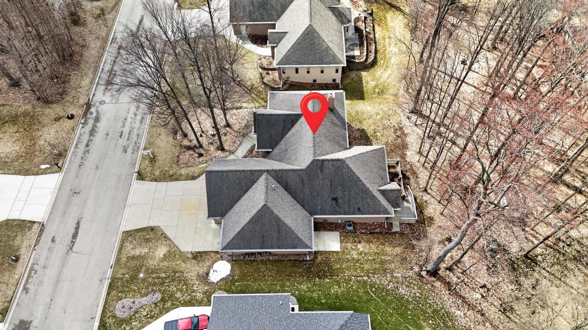 Aerial view of a house marked by a red location pin, surrounded by leafless trees.