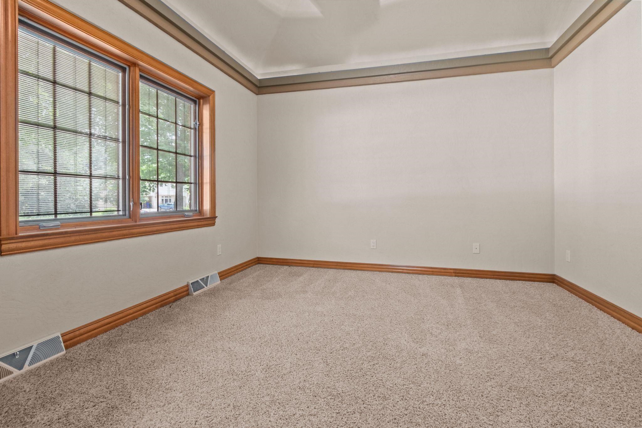 Empty carpeted room with large wood-trimmed windows and a tray ceiling.