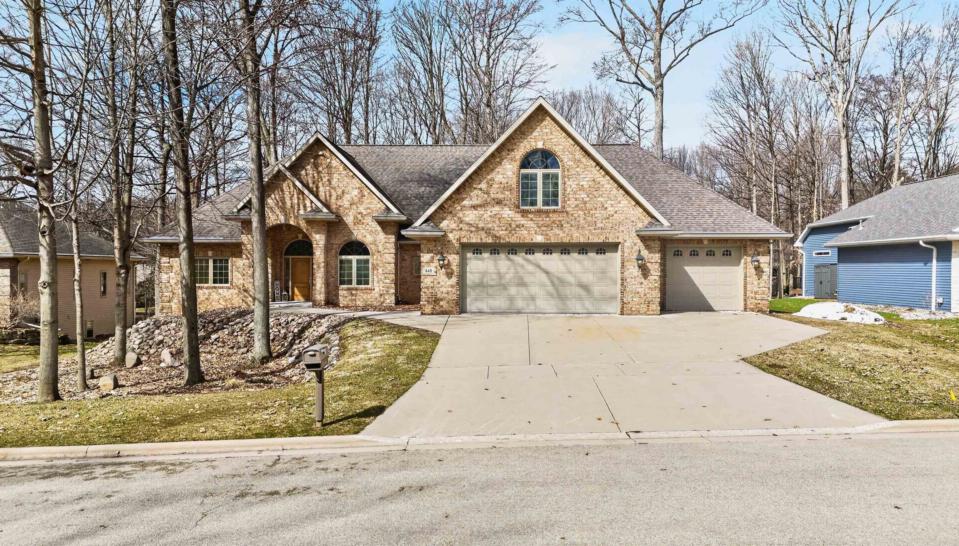 Tan brick home with multiple gables, an arched entry, and a wide driveway.