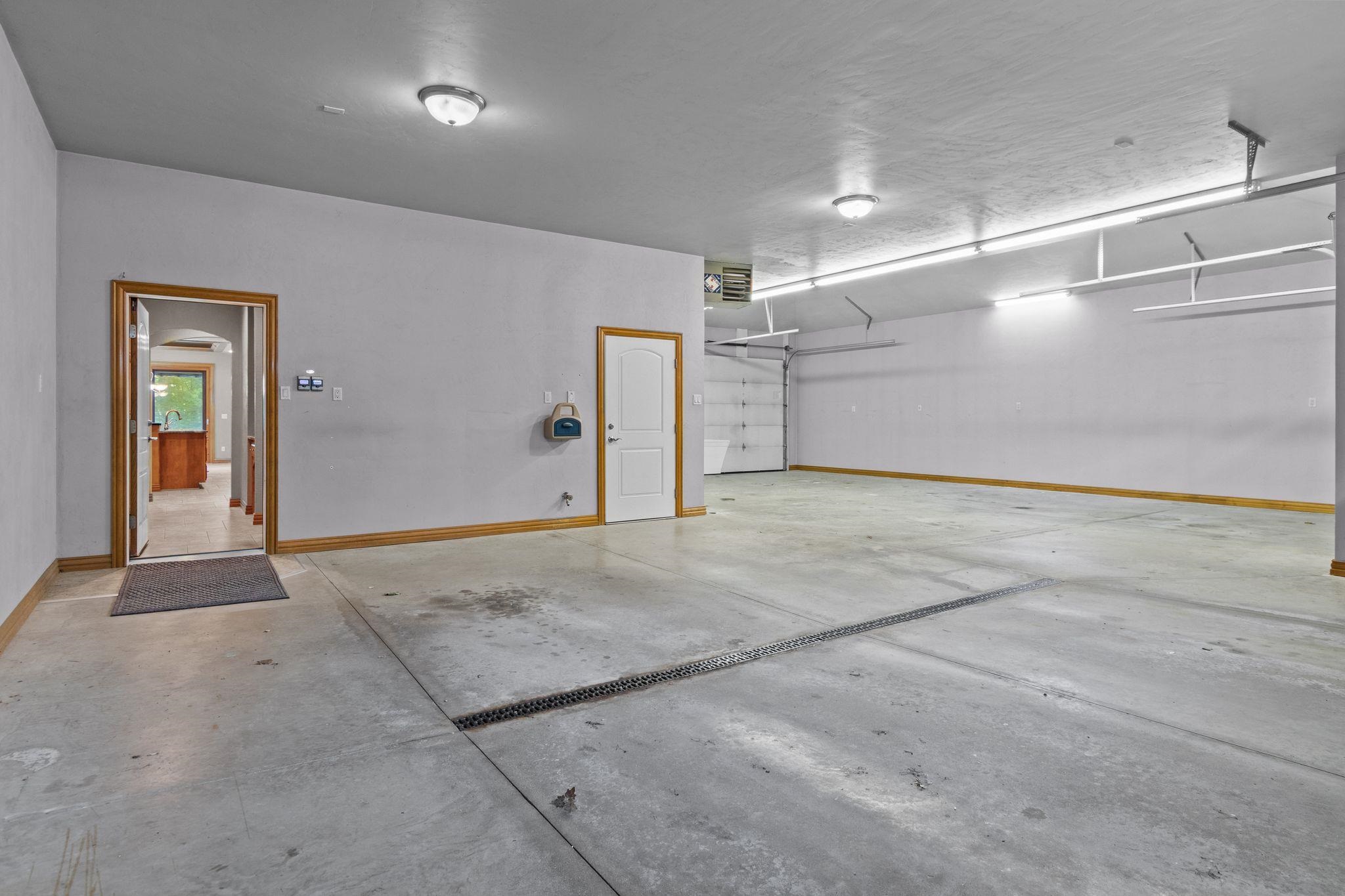 Spacious garage with a concrete floor drain, overhead doors, and an entry doorway.
