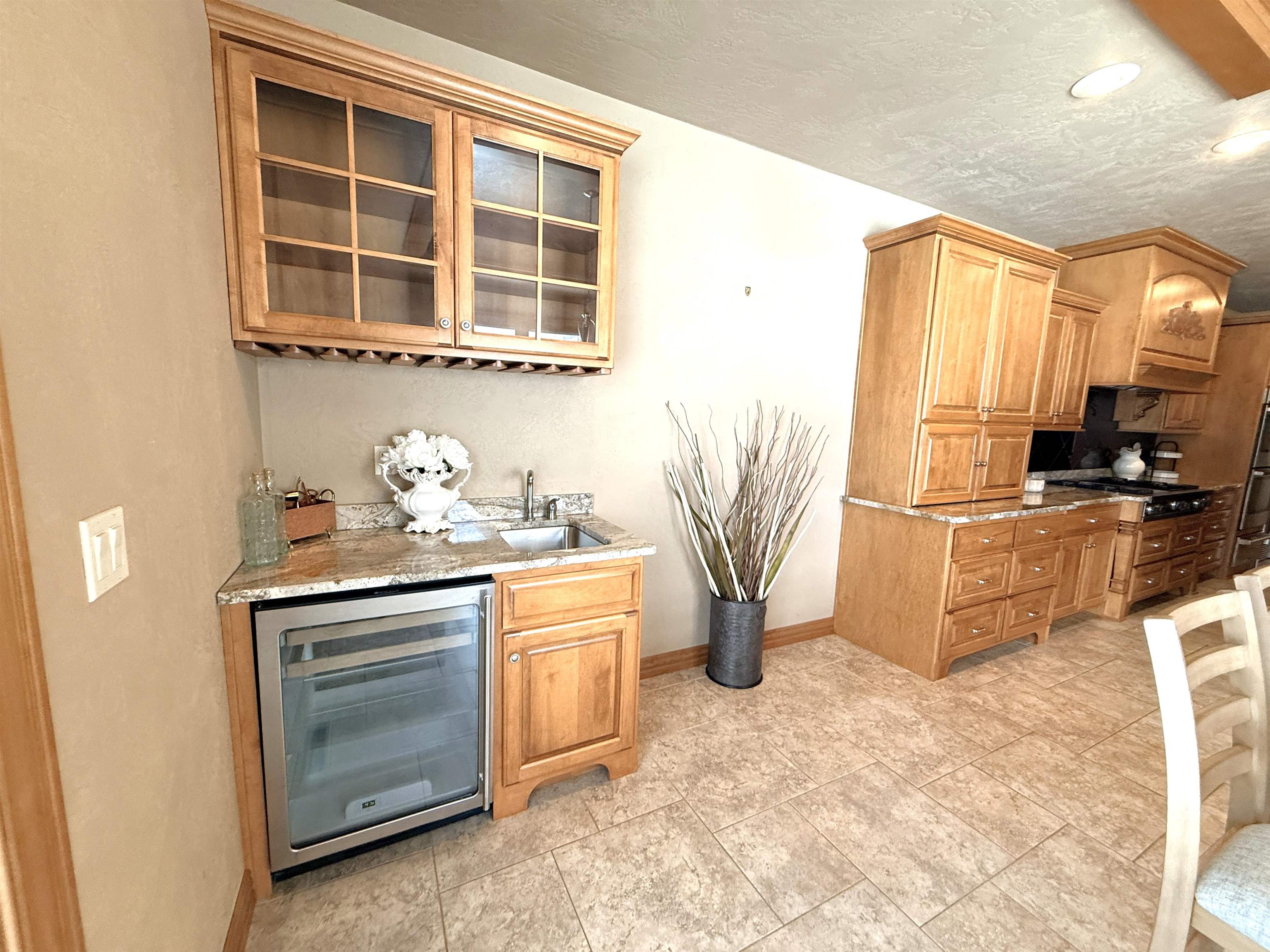 Kitchen with honey-colored cabinets, a stone counter, a small sink, and a glass-front wine refrigerator.