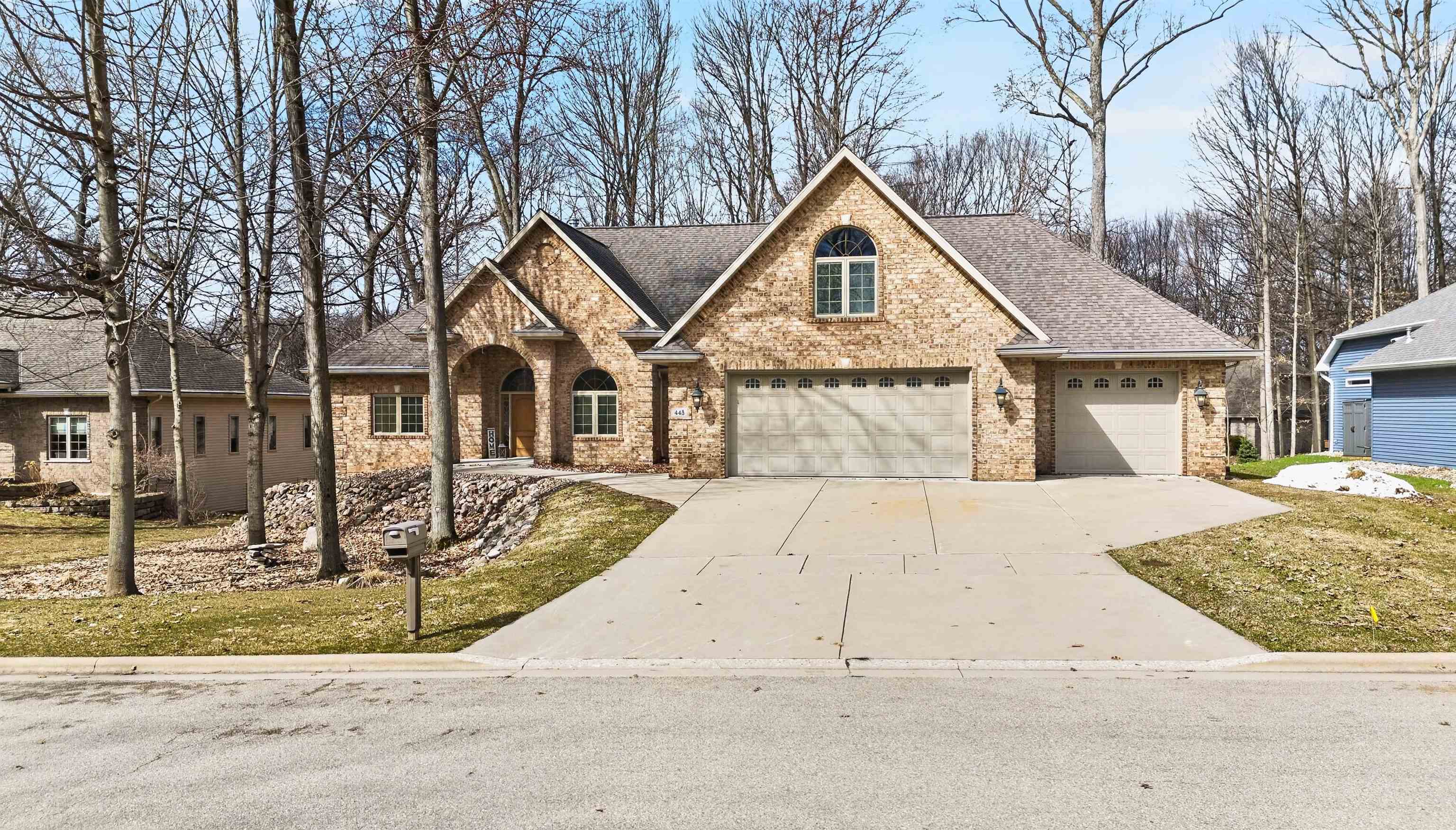 Tan brick house with multiple gables, an arched entrance, and a wide driveway.