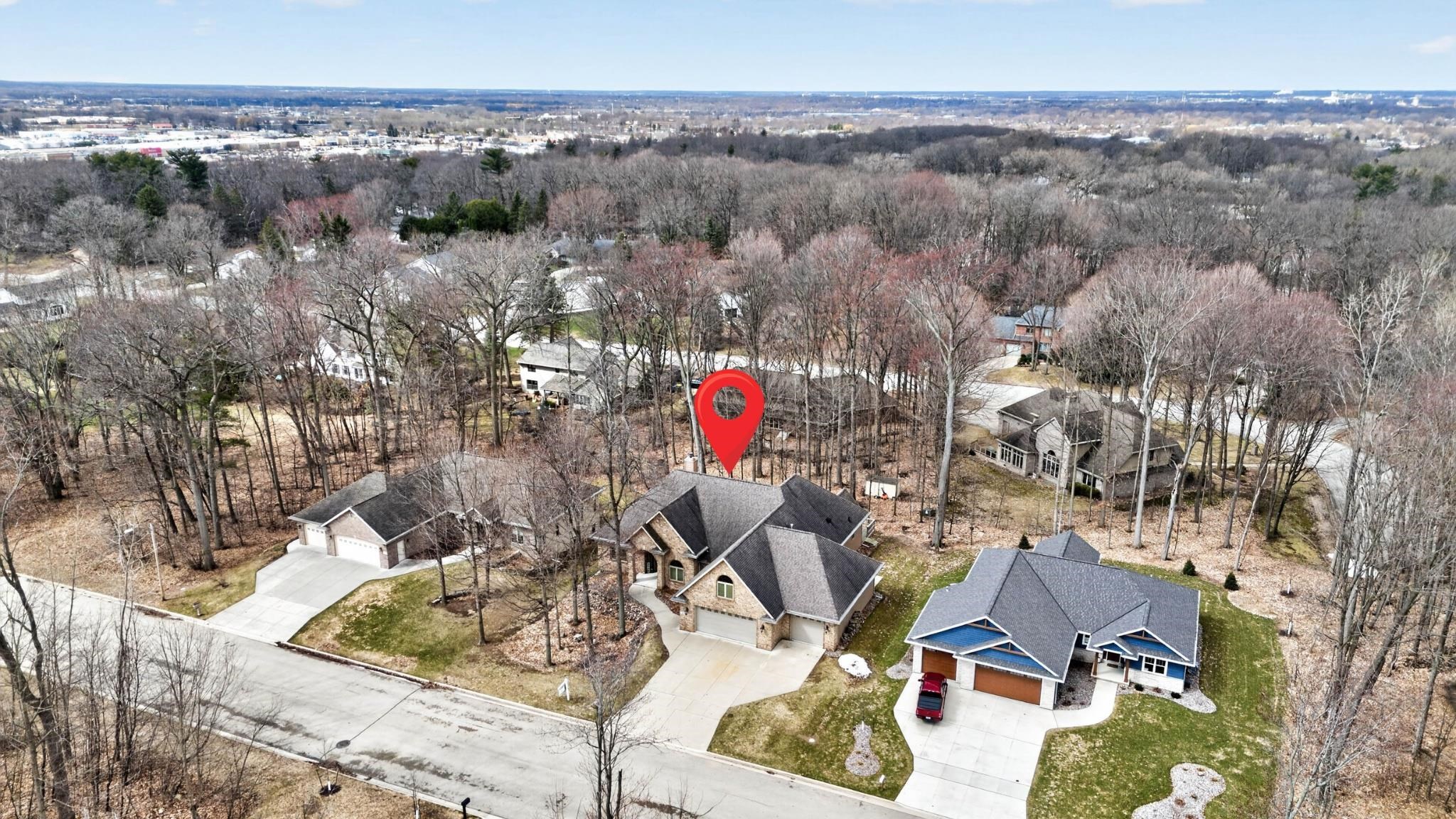 Aerial view of a wooded lot marked by a red pin among neighborhood homes.