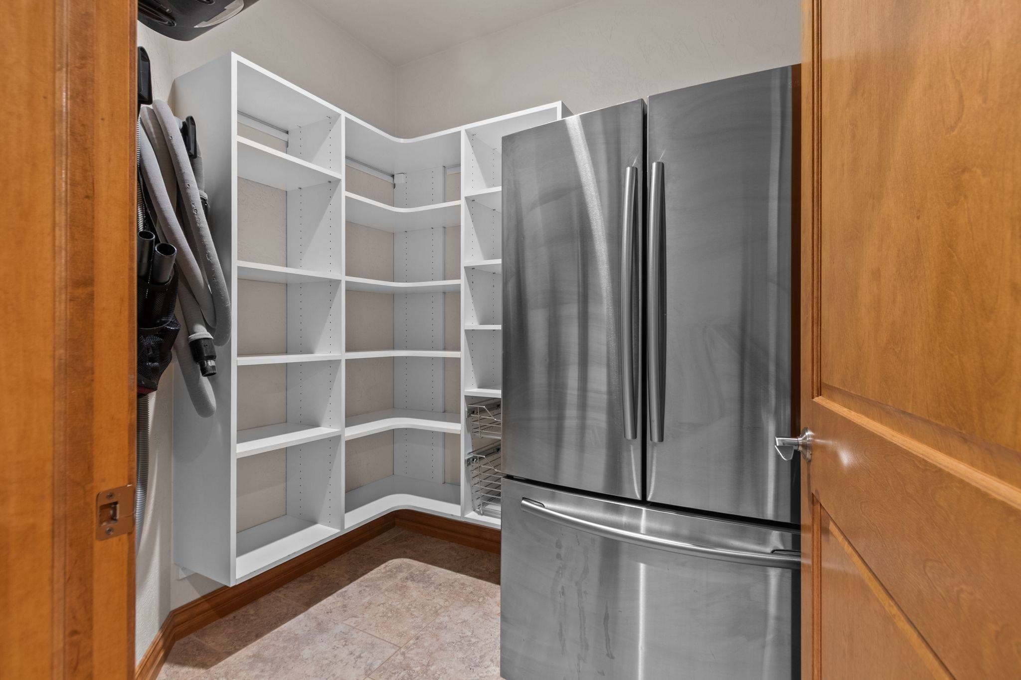 Pantry with wraparound shelving and a stainless steel refrigerator.