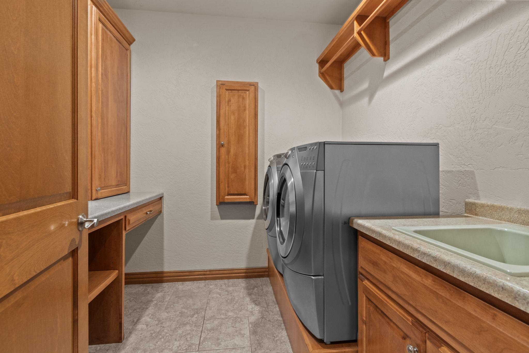 Laundry room with front-loading washer and dryer, wooden cabinets, and a utility sink.