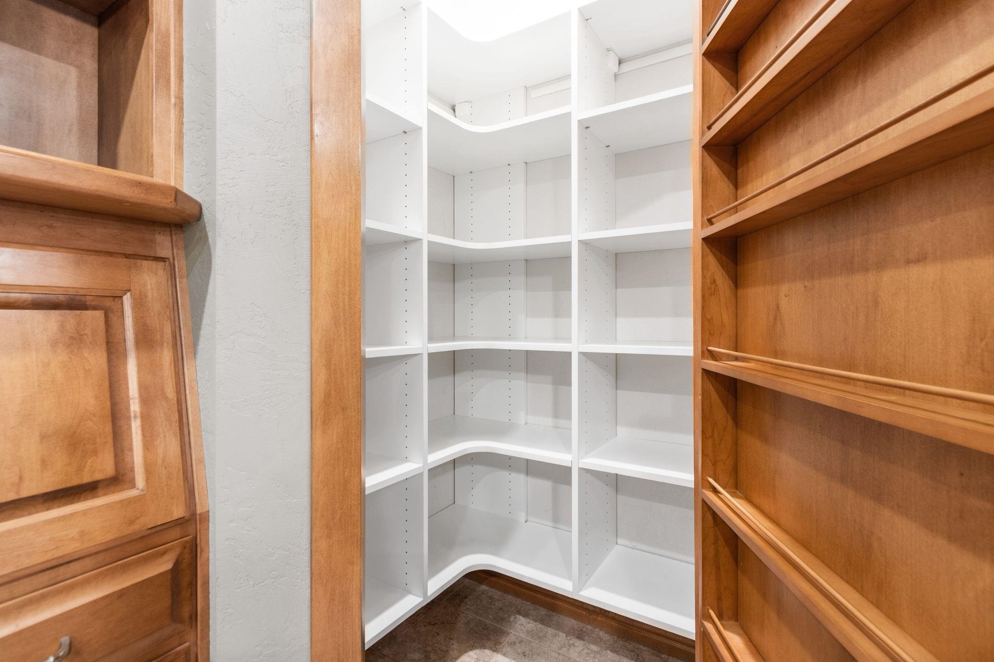 Walk-in closet with empty white corner shelves, wood shelving, and a paneled wood door.