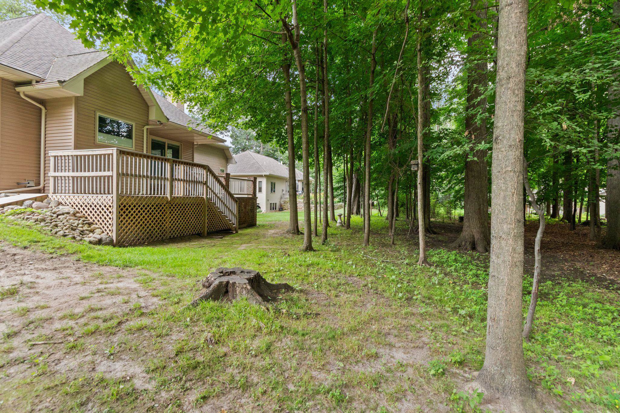 House deck overlooking a shaded backyard with mature trees and a tree stump.