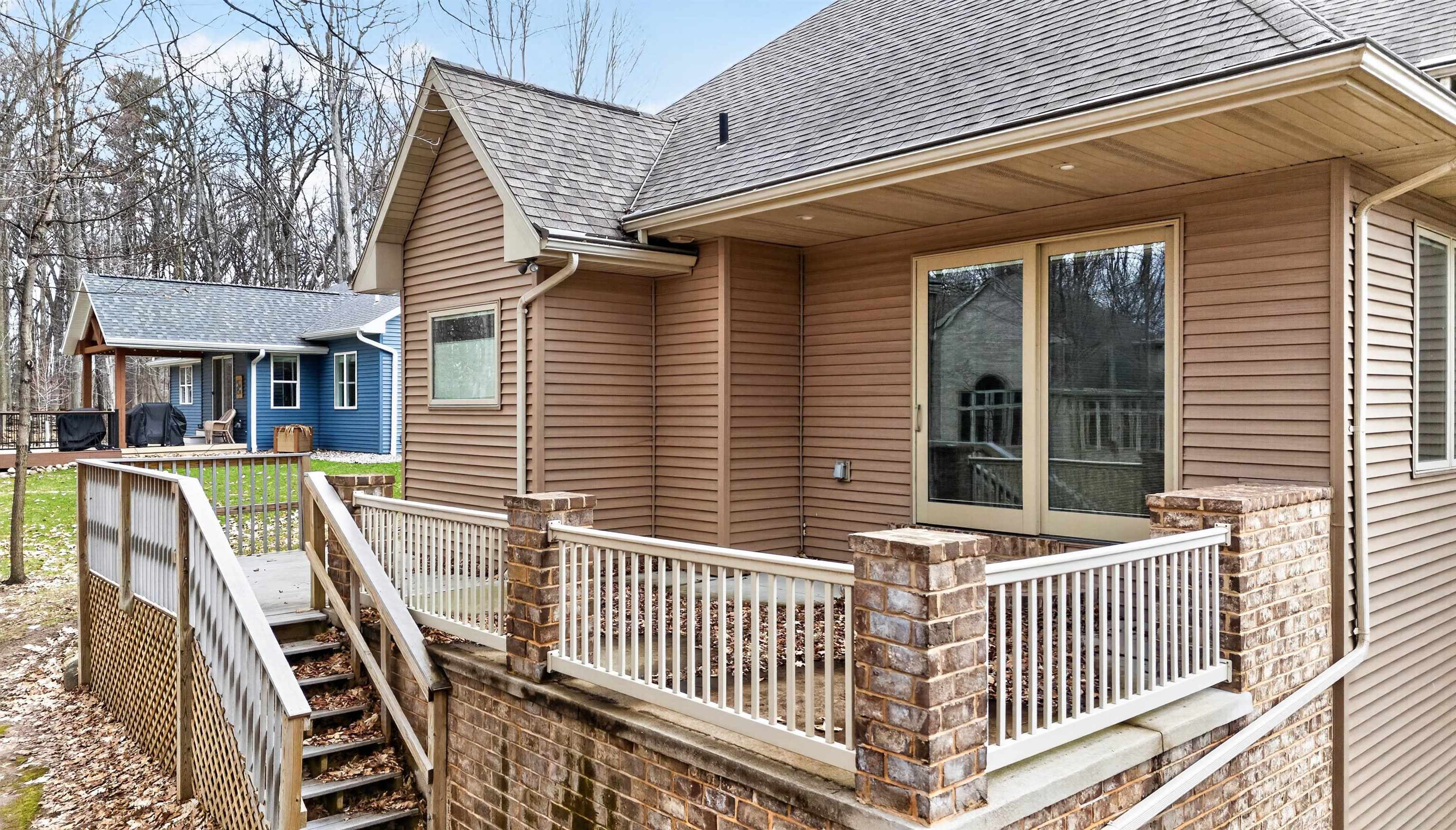 Raised brick patio with white railings and stairs beside a brown-sided home.