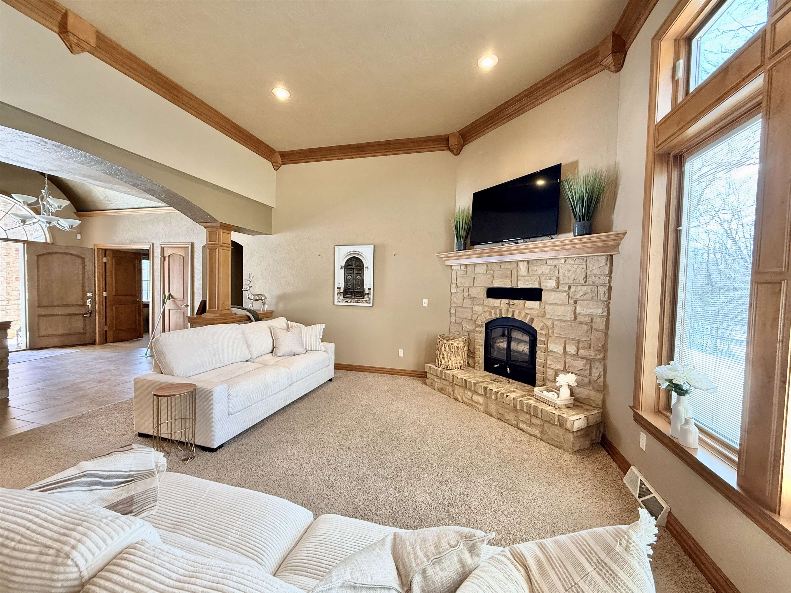 Living room with a stone fireplace, light sofas, and tall wood-trimmed windows.