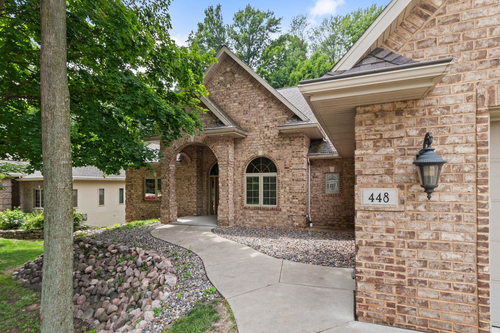 Tan brick home with an arched entry, curved walkway, and mature trees.