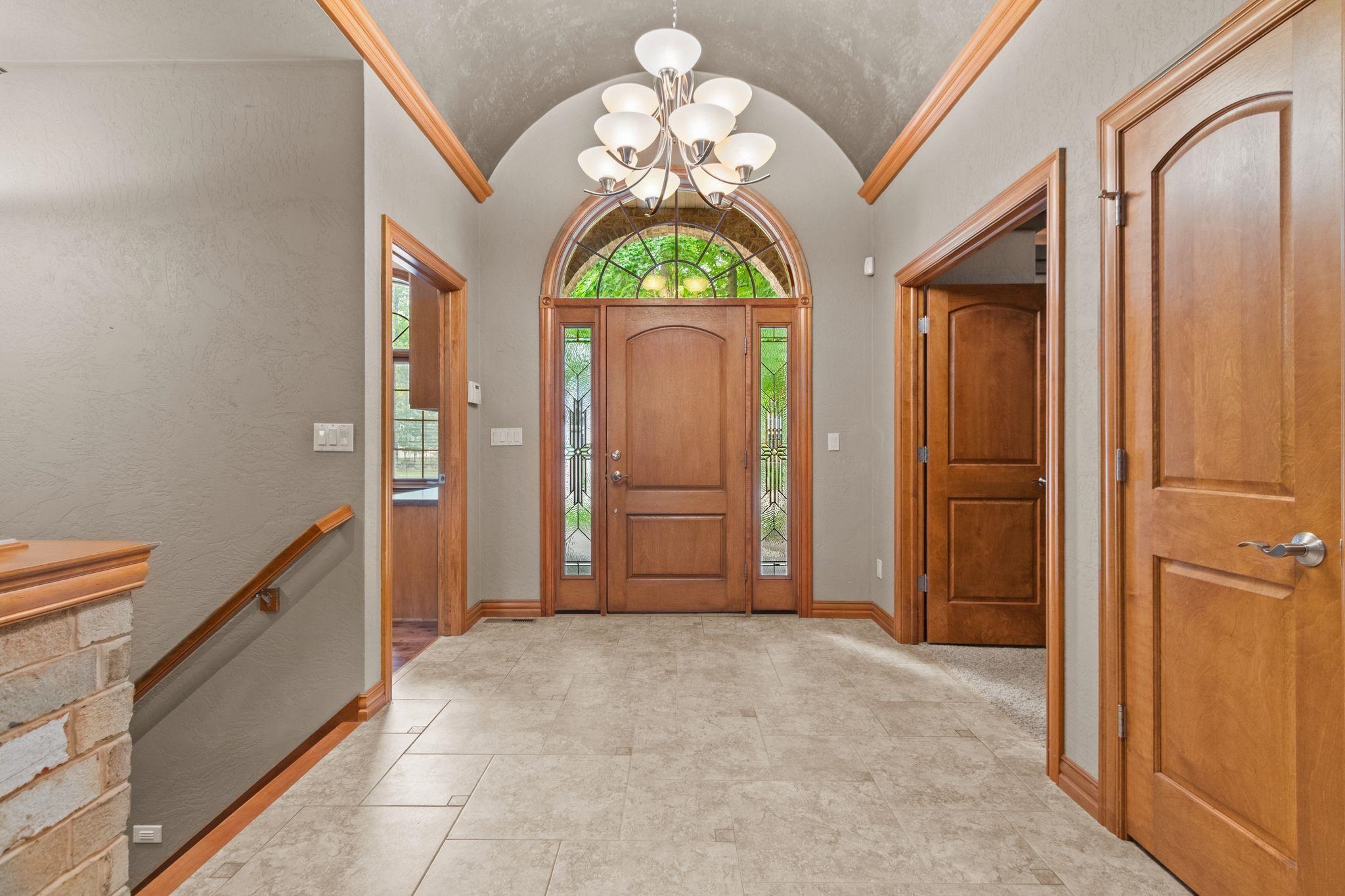 Foyer with an arched wood front door, decorative glass sidelights, tiled floor, and vaulted ceiling.