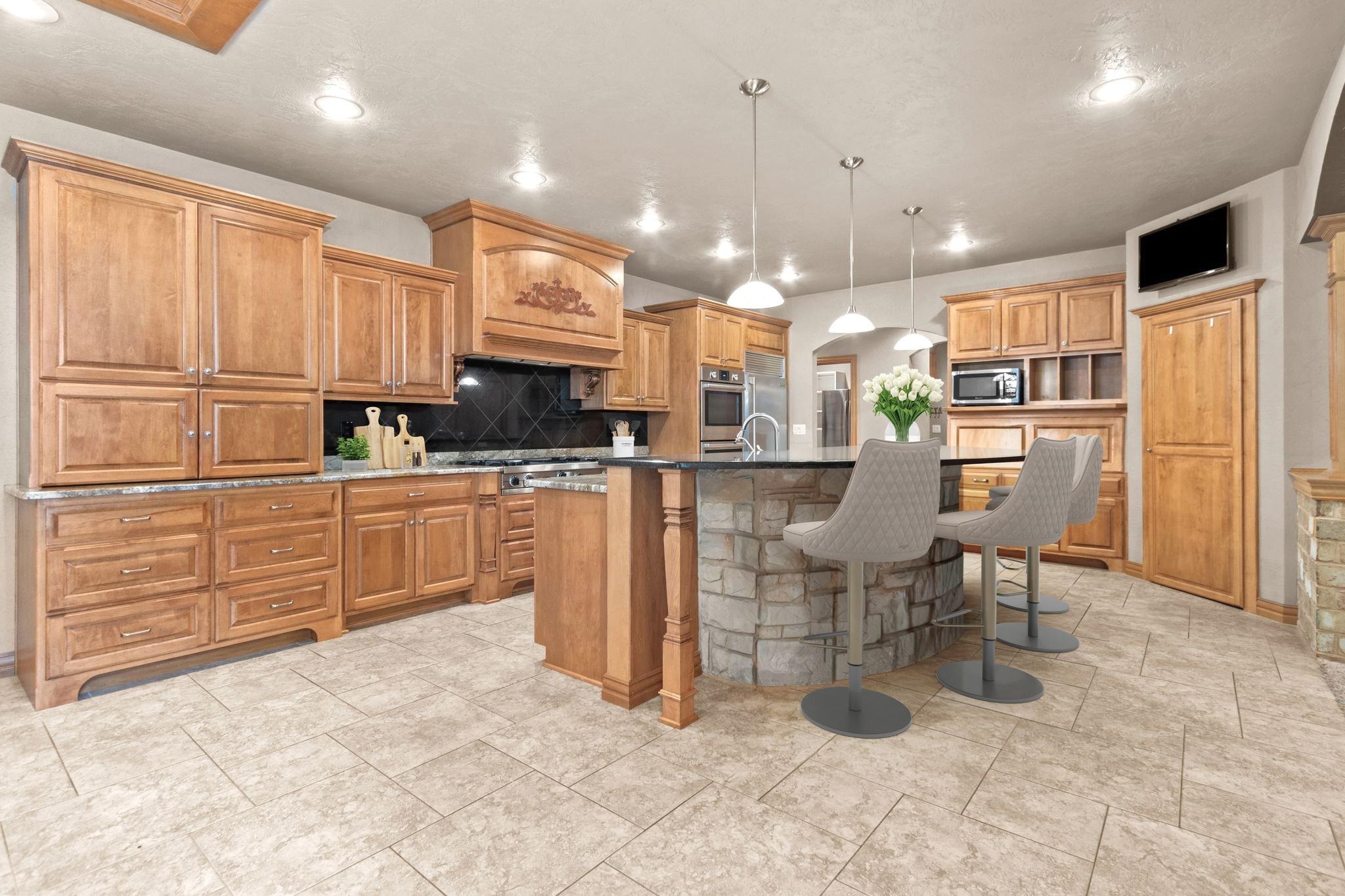 Kitchen with honey-toned cabinets, black tile backsplash, and a stone island with bar stools.