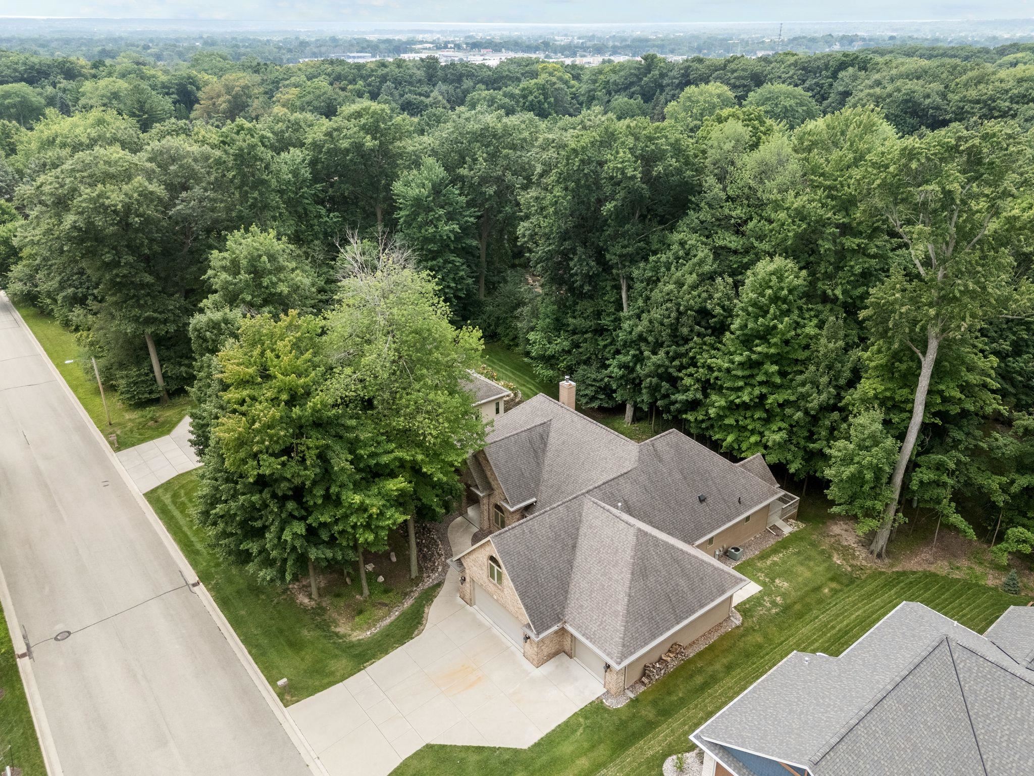 Aerial view of a tan house and driveway bordered by mature trees and dense woods.