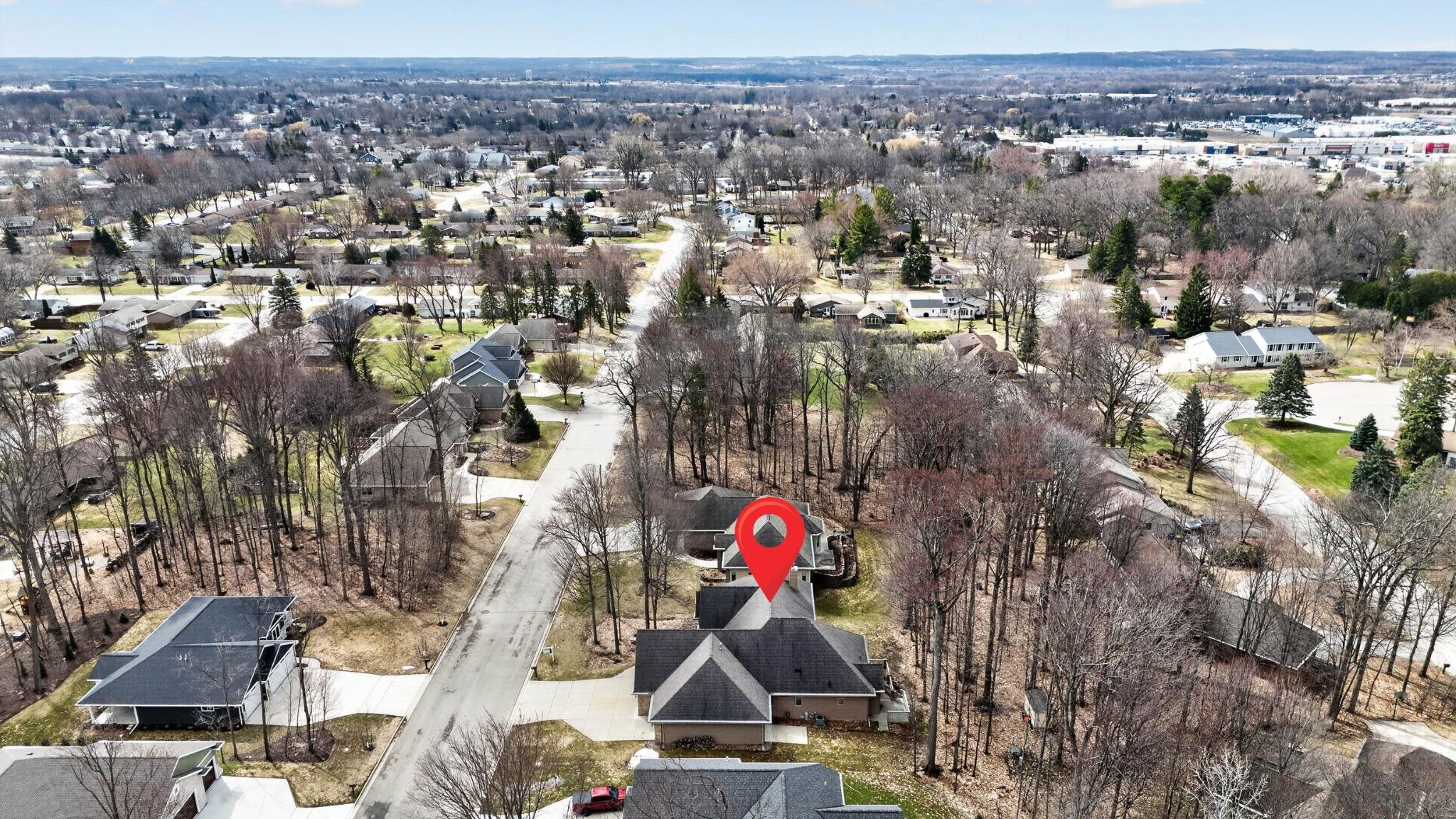 Aerial view of a house among mature trees in a Green Bay neighborhood, marked with a red pin.