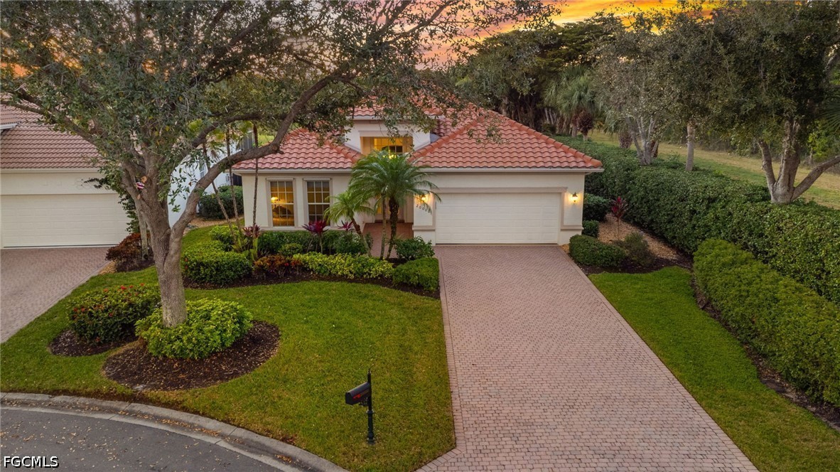 Single-story home with terracotta tile roof, attached garage, and broad paver driveway amid mature landscaping.