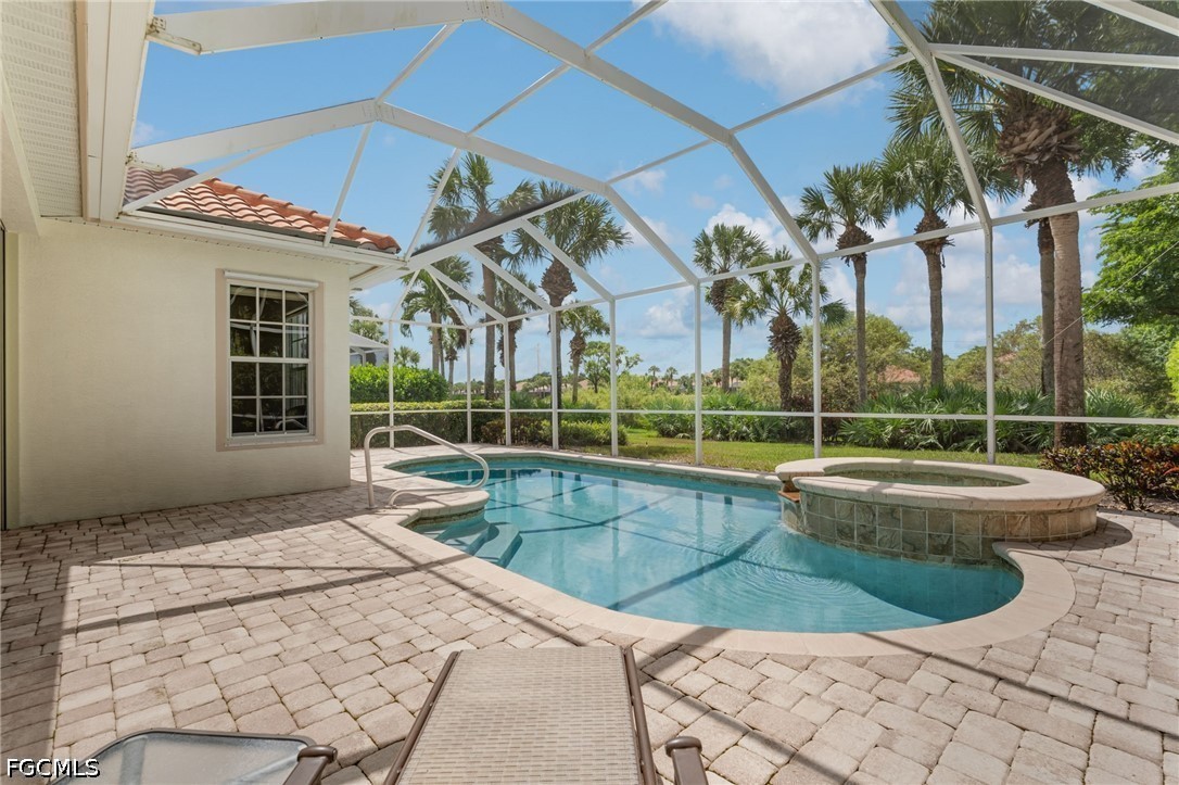 Screened pool patio with a raised circular spa, pavers, lounge chairs, and palm trees.