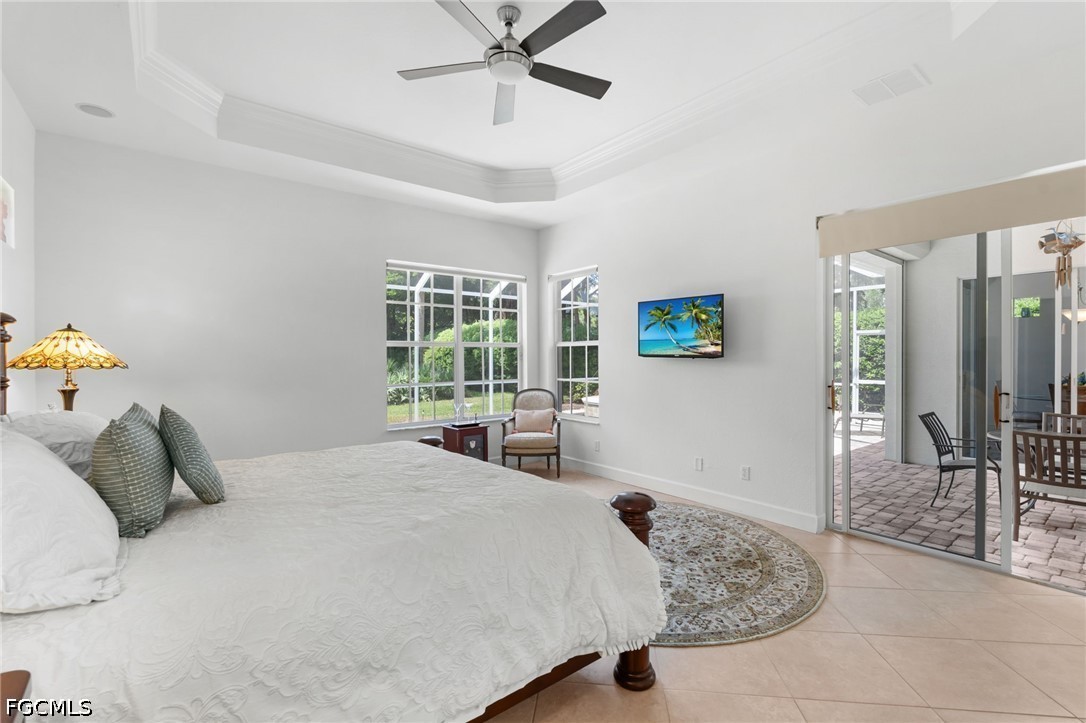 Furnished bedroom with a tray ceiling, large windows, and sliding glass doors to a patio.