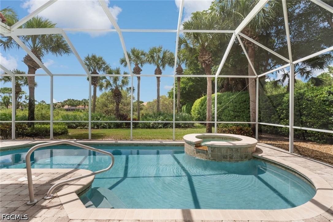 Backyard pool and raised spa beneath a screened lanai, surrounded by palms and lush landscaping.