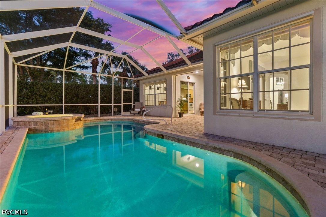 Backyard pool and raised spa beneath a screened lanai at dusk, with paved decking and outdoor seating.