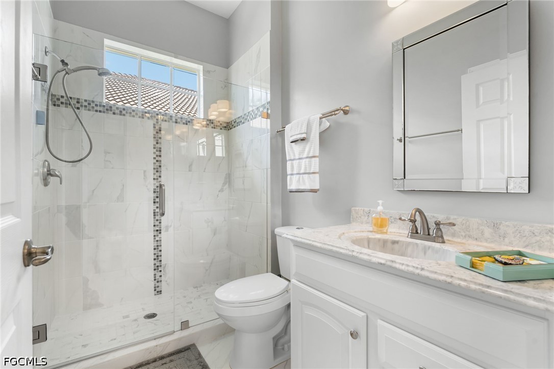 Bathroom with a glass-enclosed marble shower and white vanity with marble countertop.