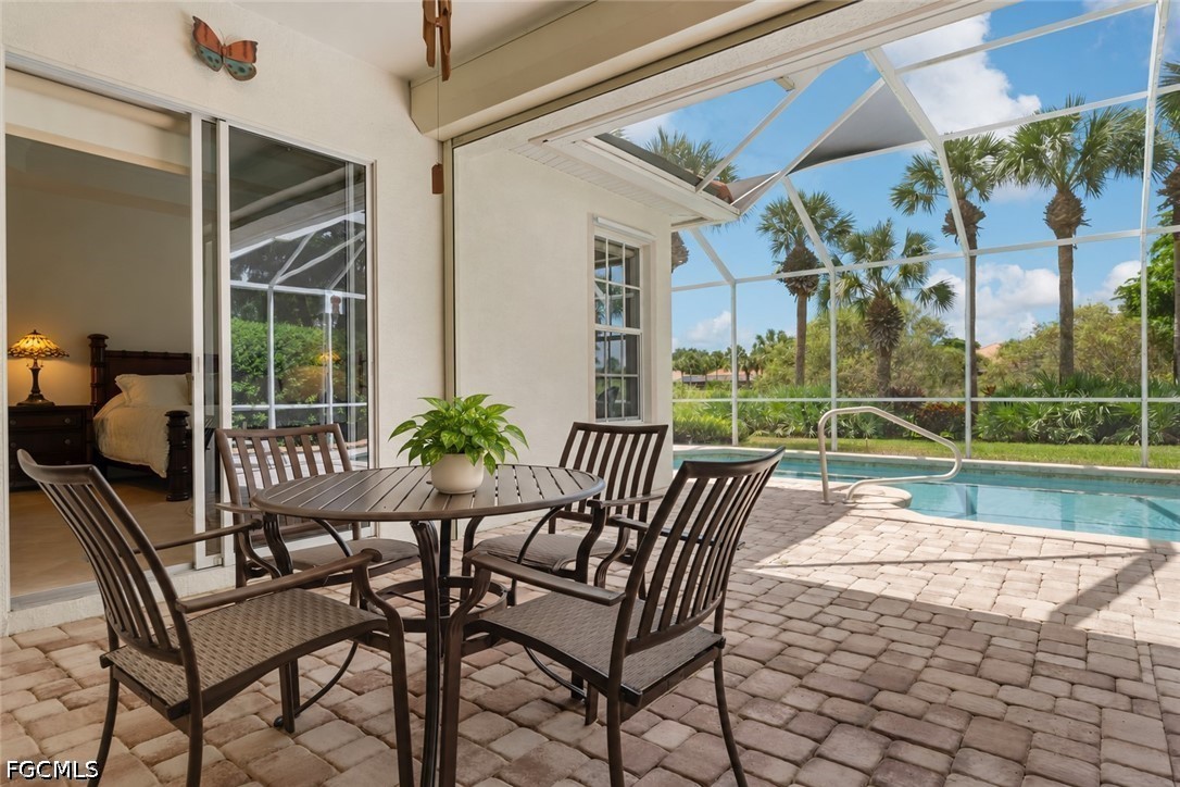 Screened patio with outdoor dining furniture beside a pool and palm trees.