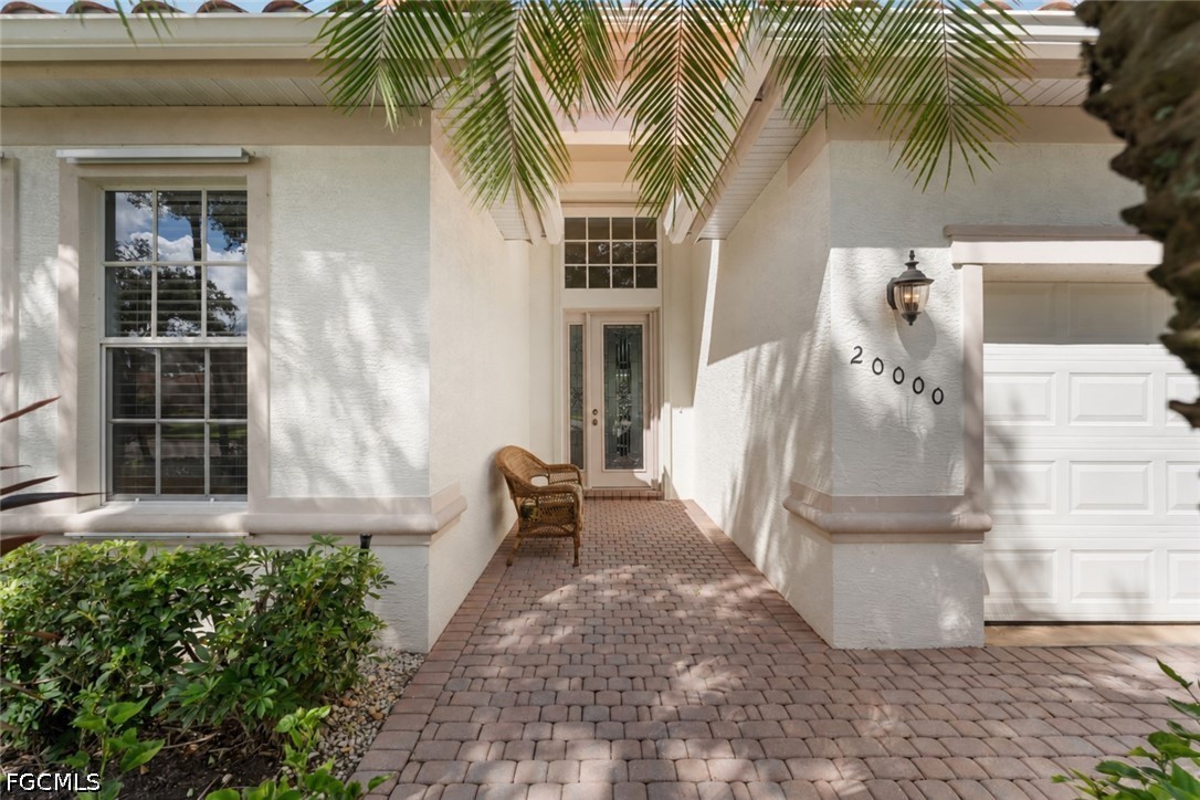 White stucco home entrance with a brick paver walkway, glass-paneled door, and attached garage.