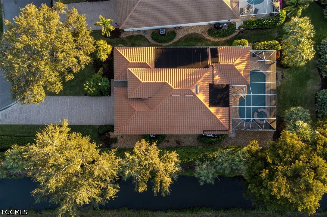 Aerial view of a tile-roofed home with a screened pool beside a waterway.