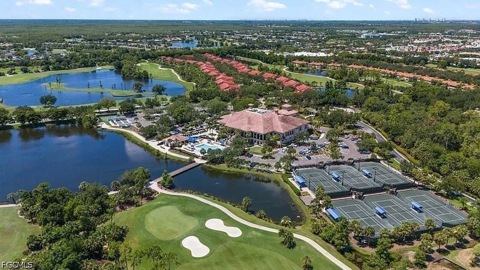 Aerial view of a community clubhouse, pool, tennis courts, golf course, and lakes.