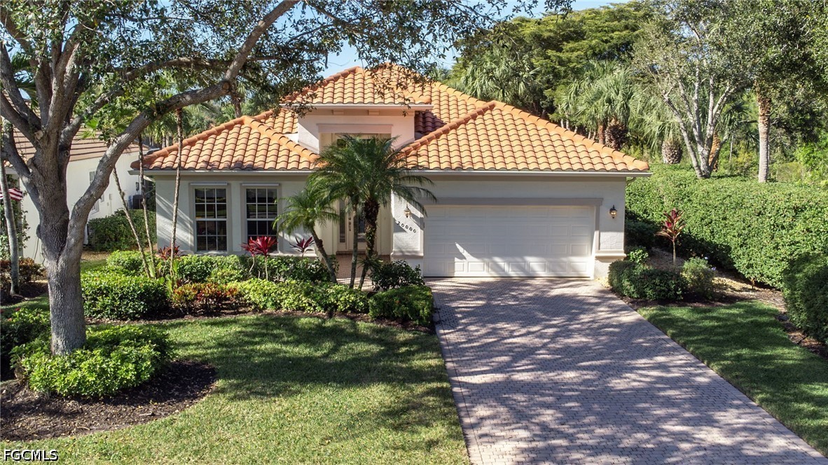Home with a terracotta tile roof, double garage, paver driveway, and mature trees framing the landscaped front yard.