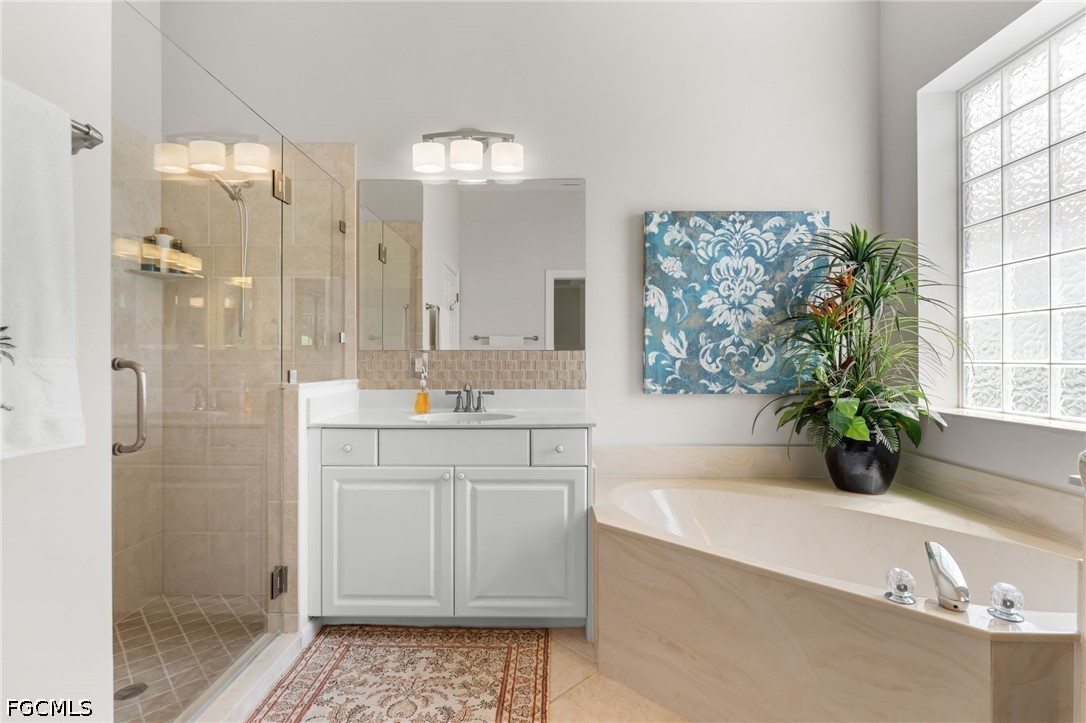 Bathroom with glass shower, white vanity, and built-in corner tub beside a glass-block window.