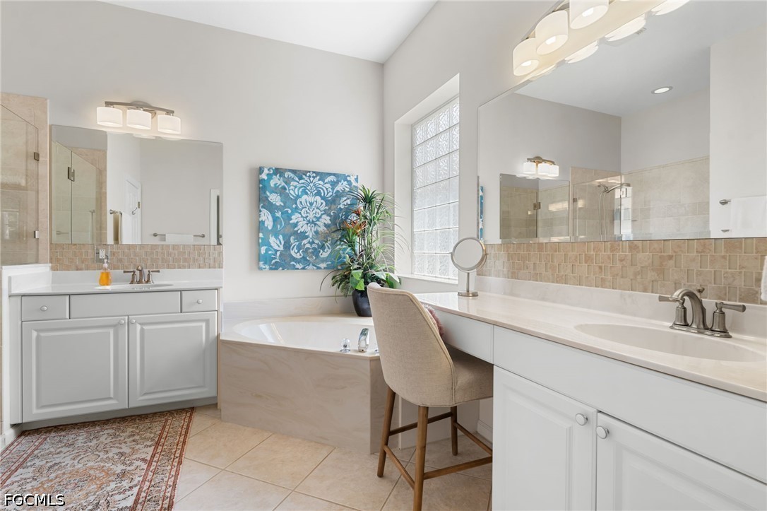 Primary bathroom with a soaking tub, double vanity, glass-block window, and chair at the counter.