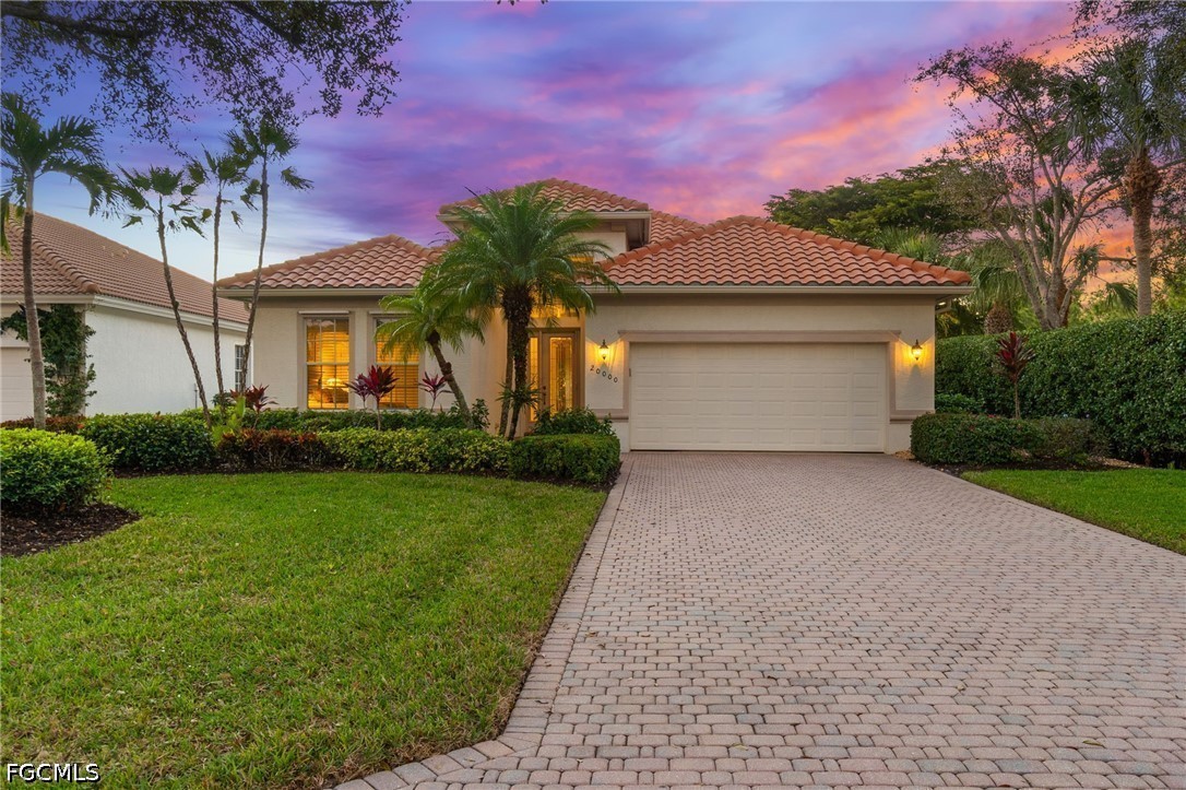 Single-story stucco home with a tiled roof, double garage, and paver driveway at sunset.
