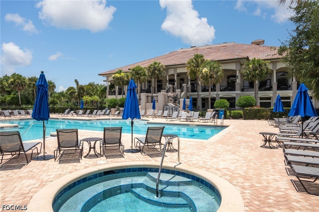 Community pool and circular spa with blue umbrellas and a two-story clubhouse.