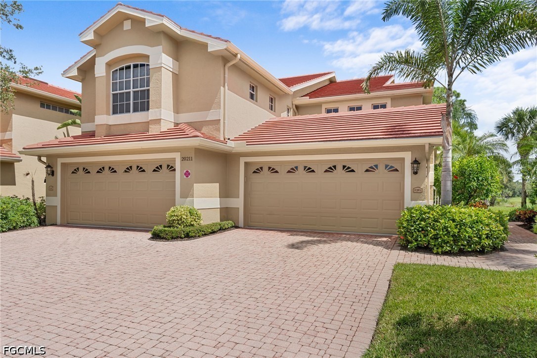 Two-story stucco home with red tile roofs, two garages, and a broad paver driveway.