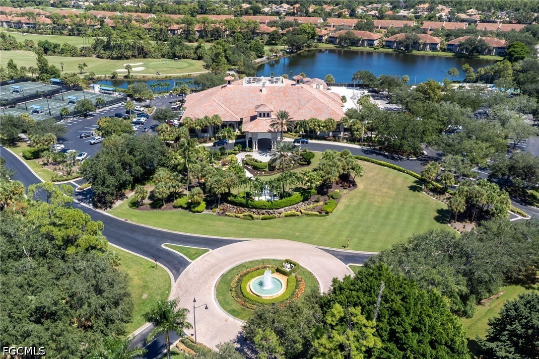 Aerial view of a community clubhouse beside a lake, with tennis courts and a fountain at the entrance.